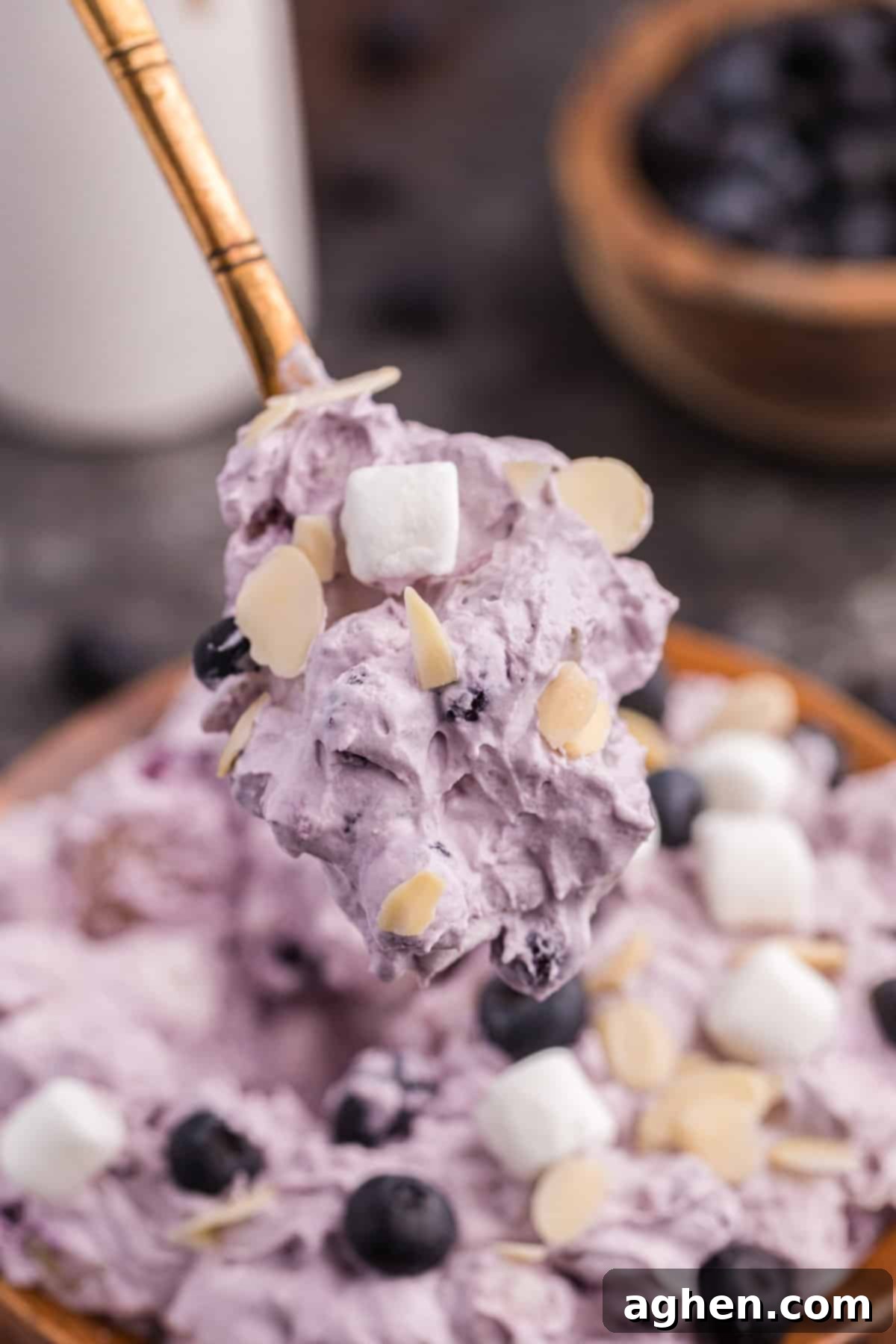 Spoonful of fluffy blueberry salad being lifted out of a bowl, showing its creamy and airy texture.