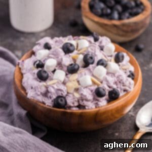 Blueberry fluff salad in a wooden bowl, topped with mini marshmallows, fresh blueberries, and almond slivers, showcasing its inviting presentation.