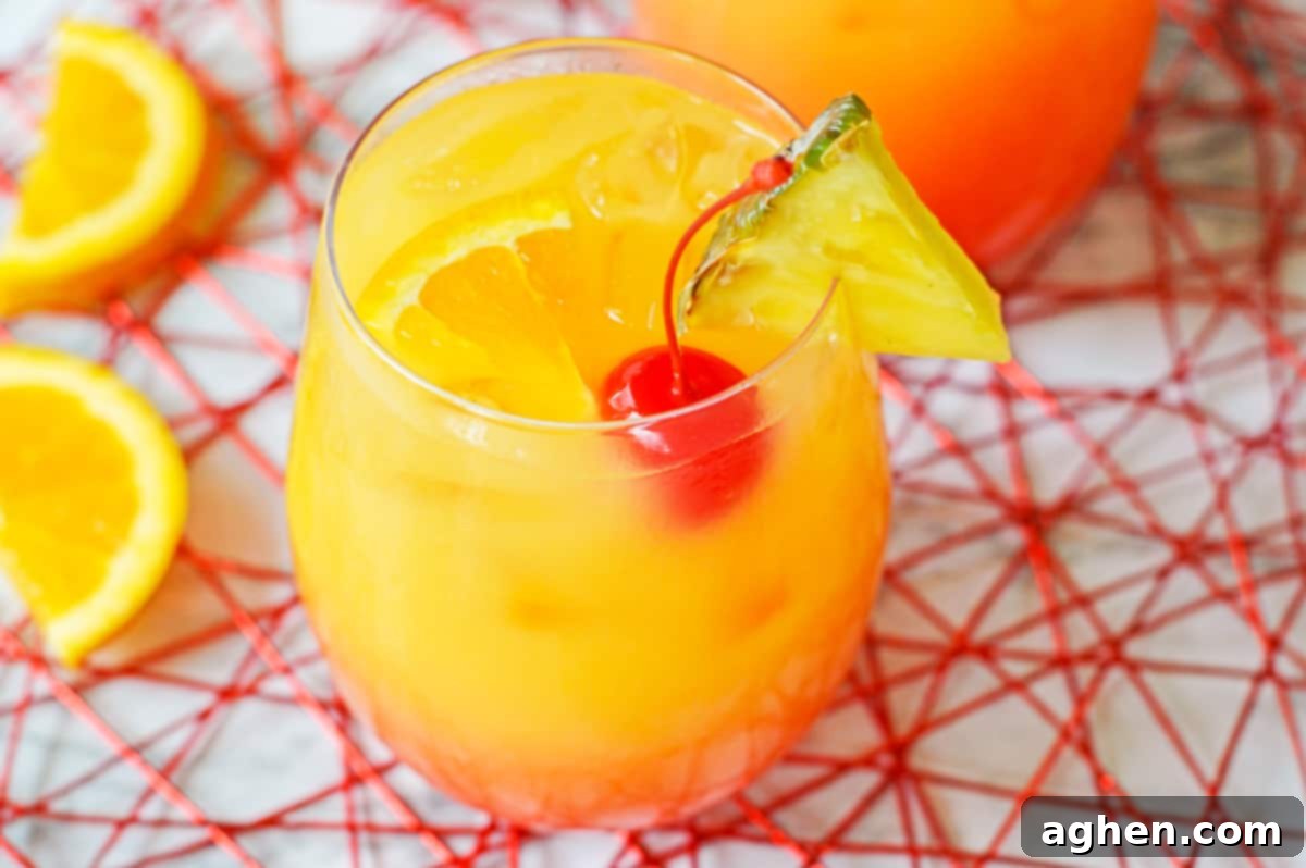 Yellow, orange, and red ombre cocktail garnished with cherry , orange, and pineapple.