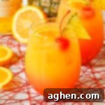 Yellow, orange, and red cocktail with cherry, pineapple, and oranges.