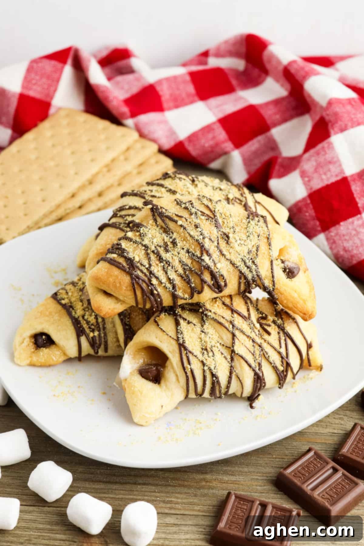 Crescent roll s'mores on white plate with graham crackers, marshmallows, and chocolate around it.