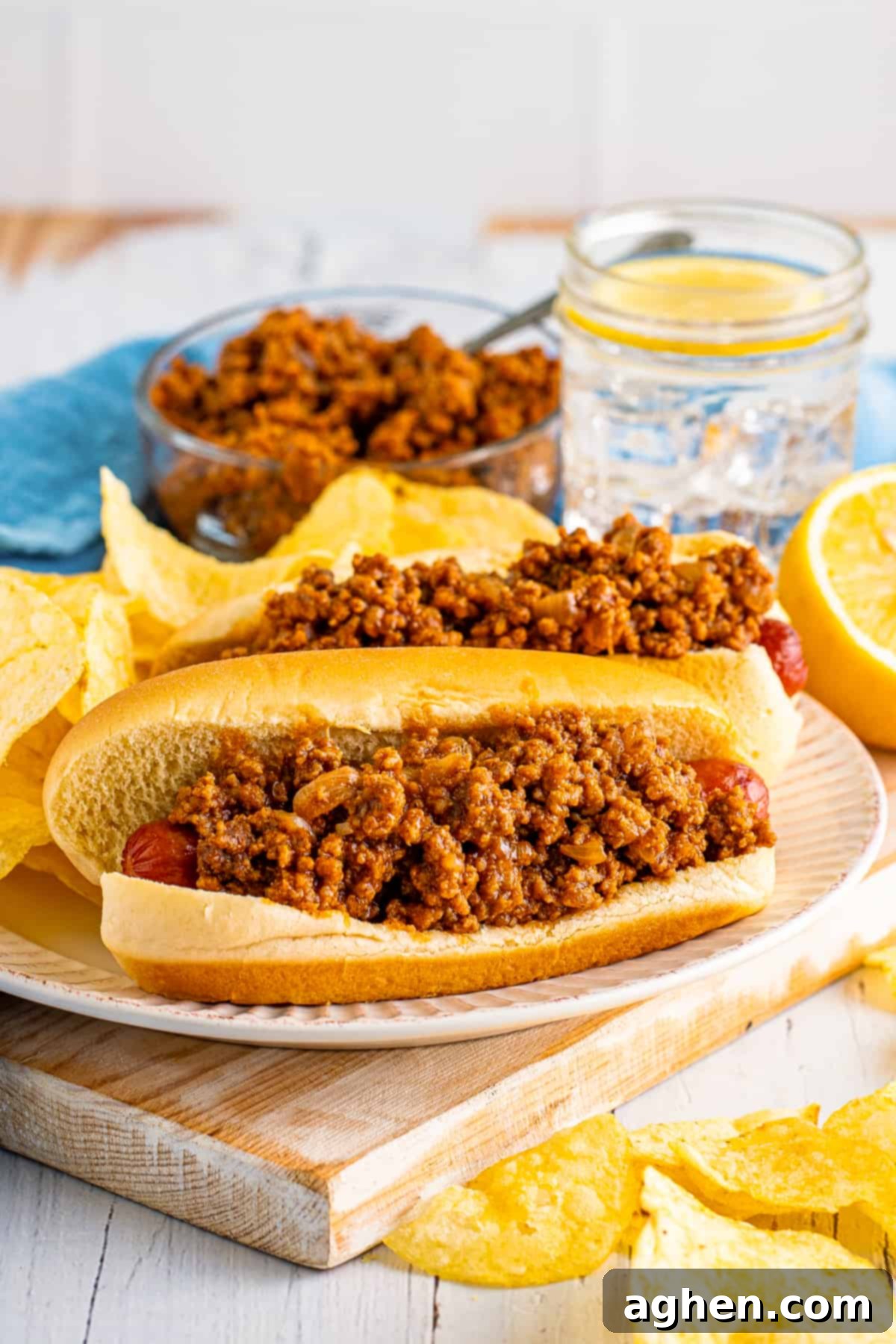 Homemade hot dog chili sauce on top of two hot dogs served with potato chips.