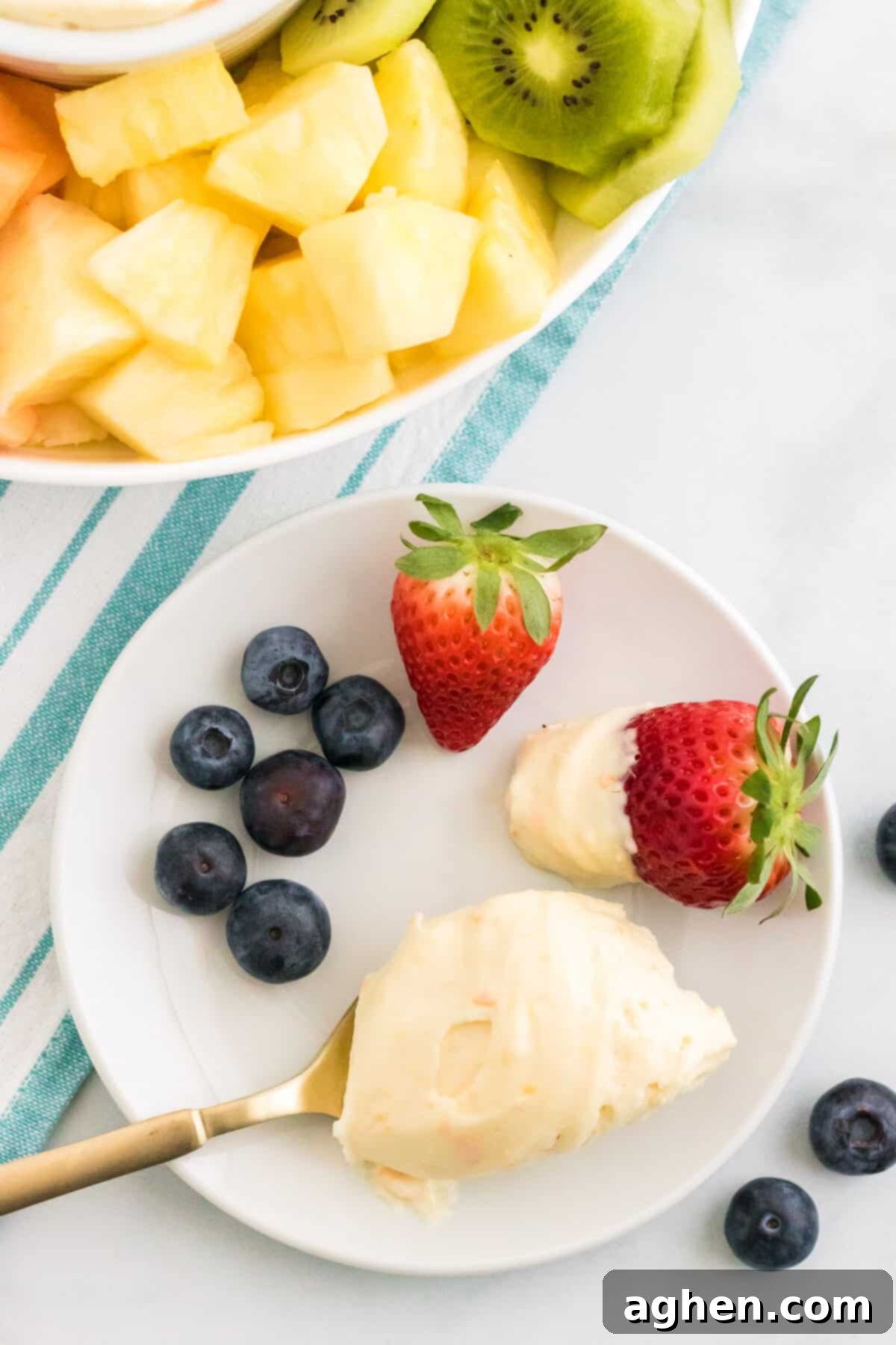 Spoonful of creamsicle fruit dip on a white plate with fresh fruit.