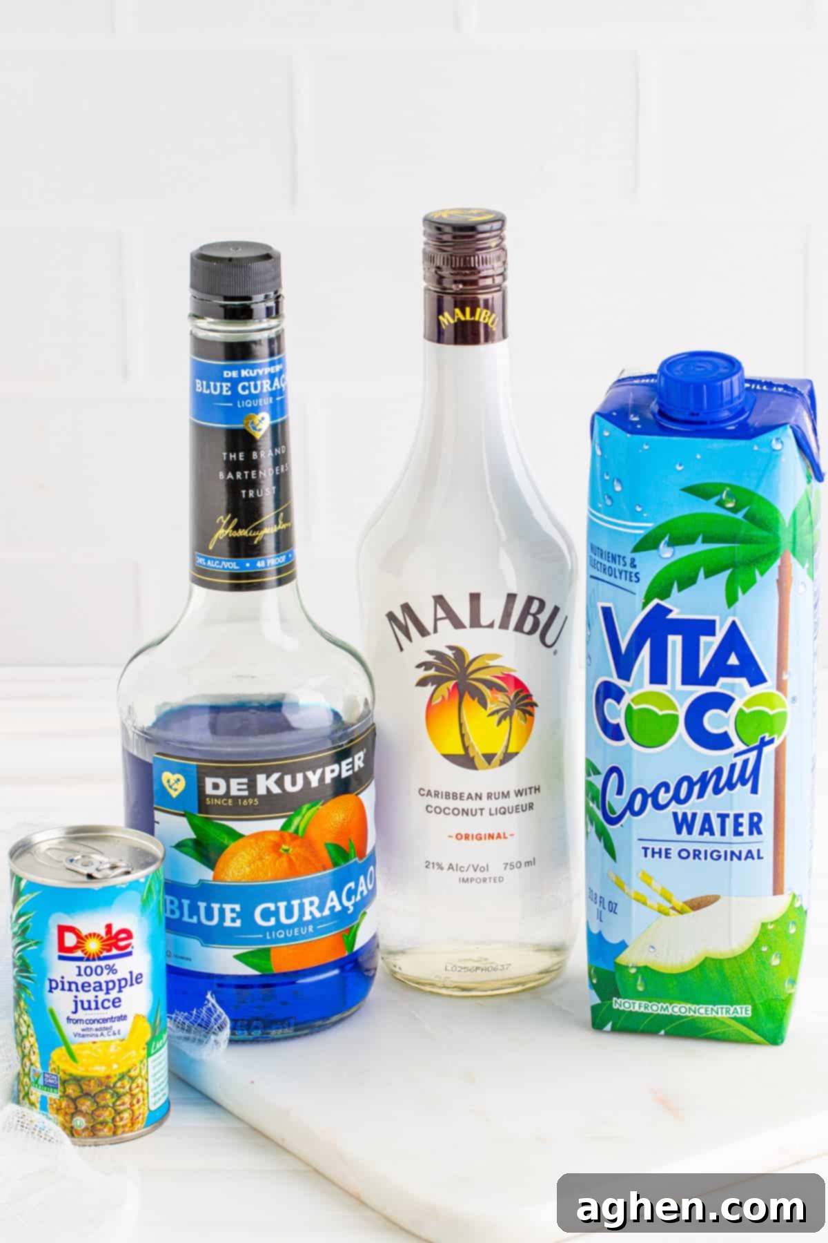 Individual ingredients for Ocean Water Cocktail: pineapple juice, Blue Curacao, Malibu coconut rum, and coconut water displayed on a white surface.