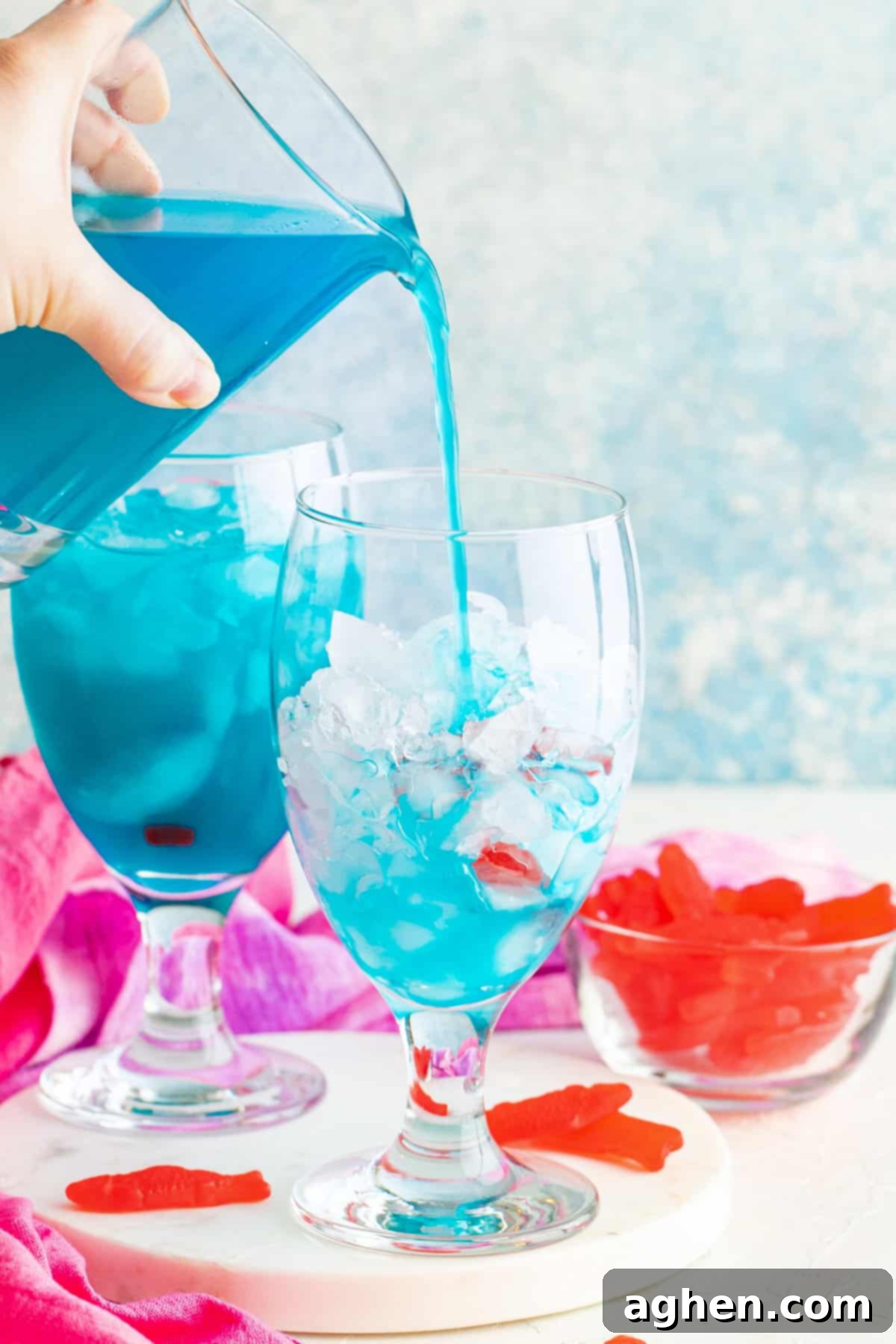 The vibrant blue drink being poured from a mixing glass into a cocktail glass filled with ice, ready for garnishing.
