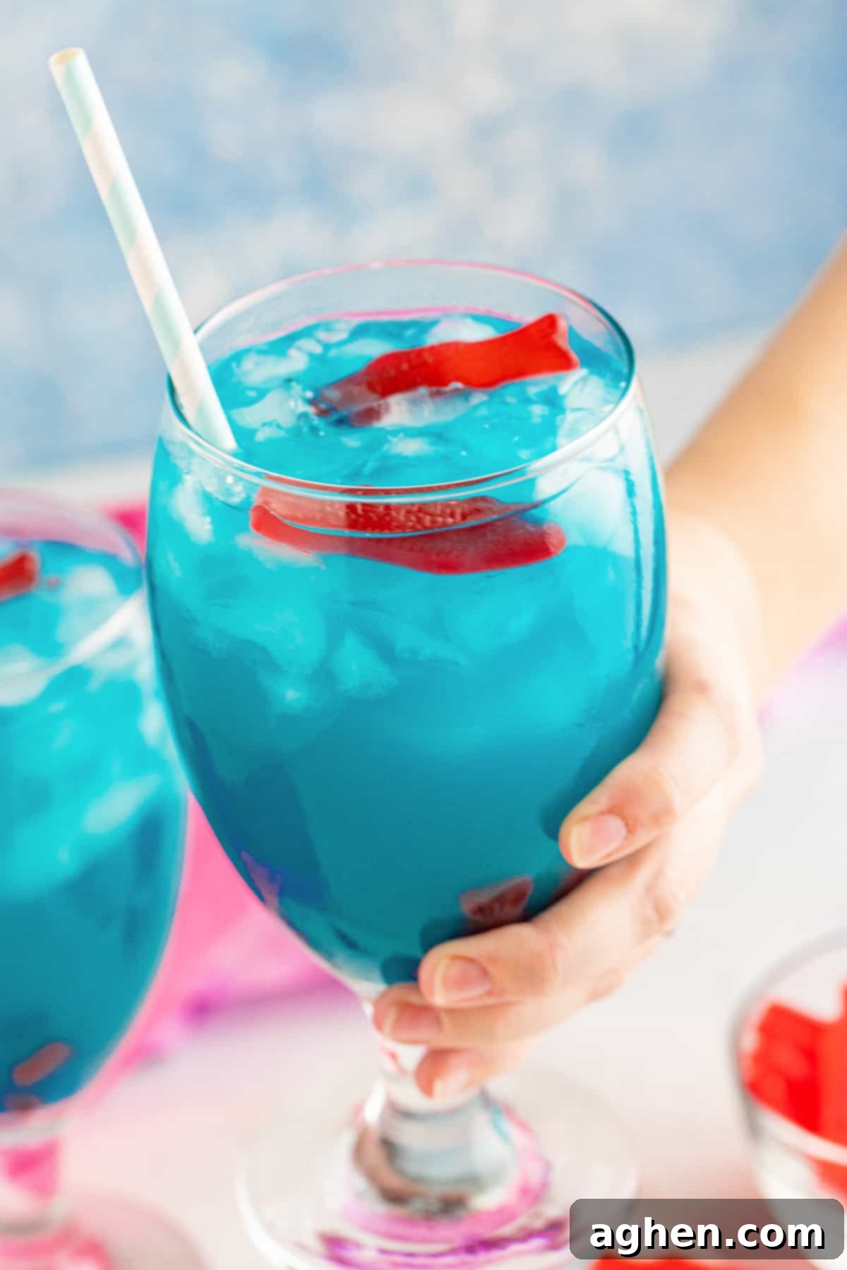 A hand holding an Ocean Water Cocktail garnished with several Swedish fish, illustrating a fun presentation.