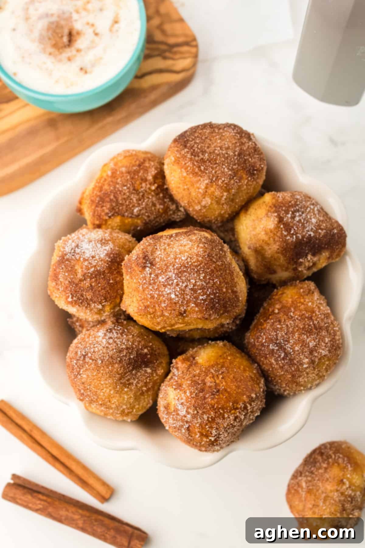 Cinnamon sugar soft pretzel bites in a white bowl with dipping sauce in the background.