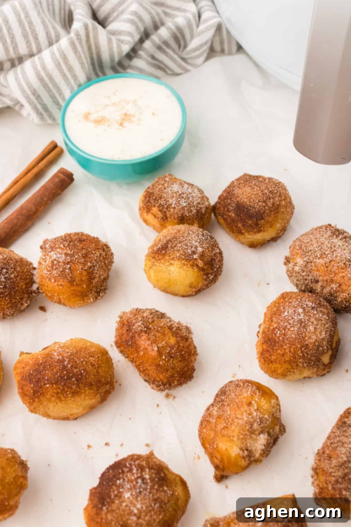 Cinnamon sugar covered pretzel bites on sheet of parchment paper with dipping sauce in the background.
