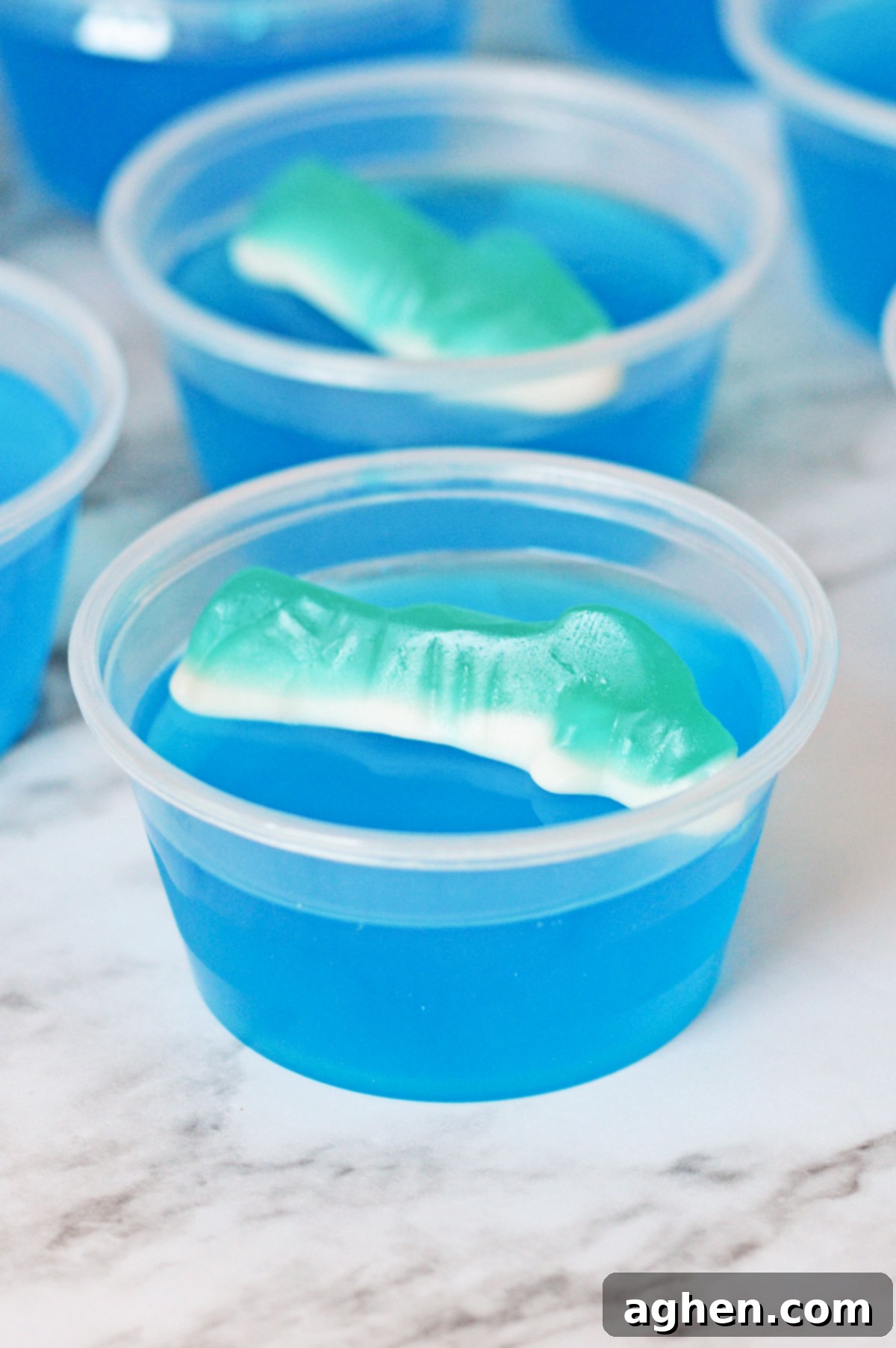 Shark jello shot with bright blue gelatin and a shark gummy candy perched on top, ready to be enjoyed.