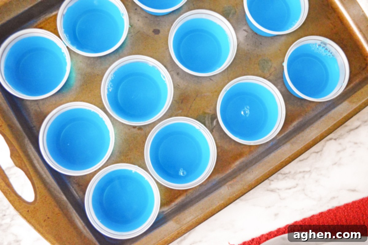 A baking sheet neatly filled with multiple blue jello shots in individual small plastic cups, ready for refrigeration.