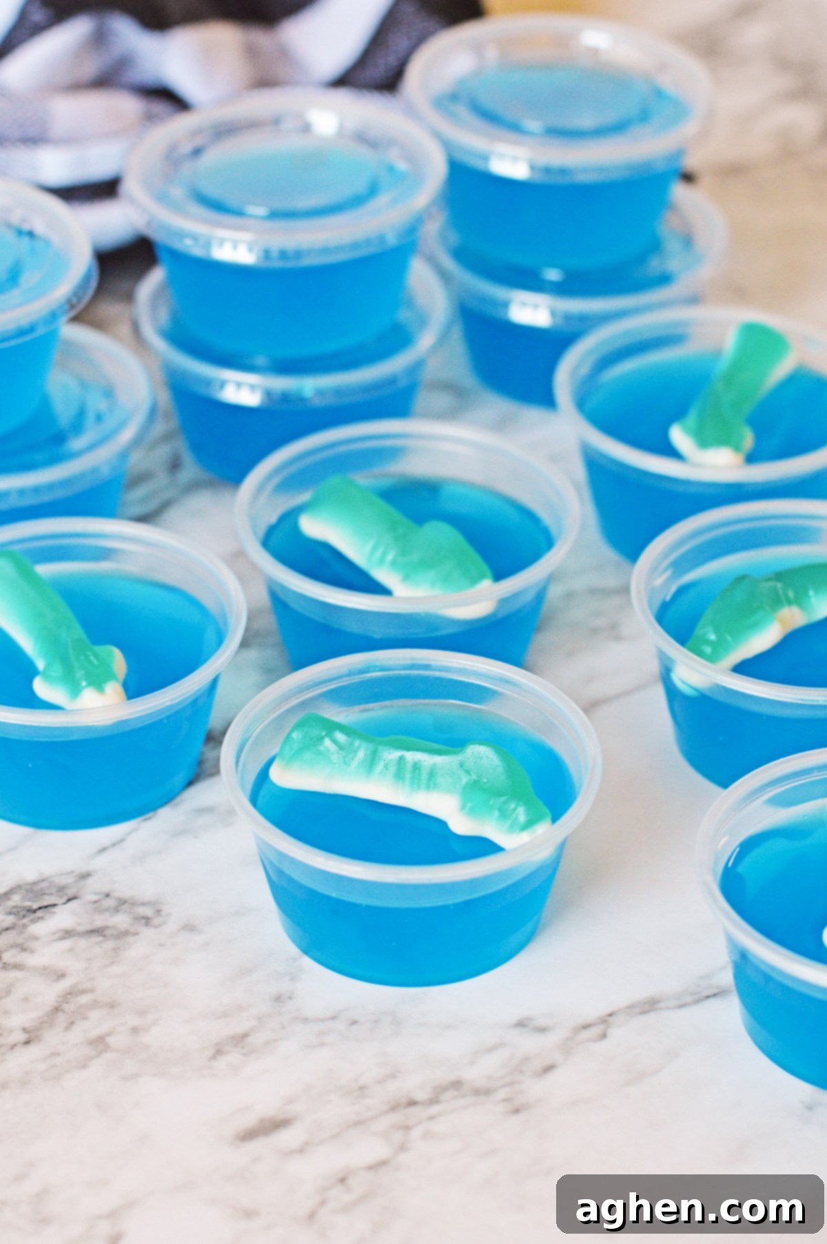 Finished shark bite jello shots, each perfectly set and topped with a colorful gummy shark, displayed in shot cups, some with lids.