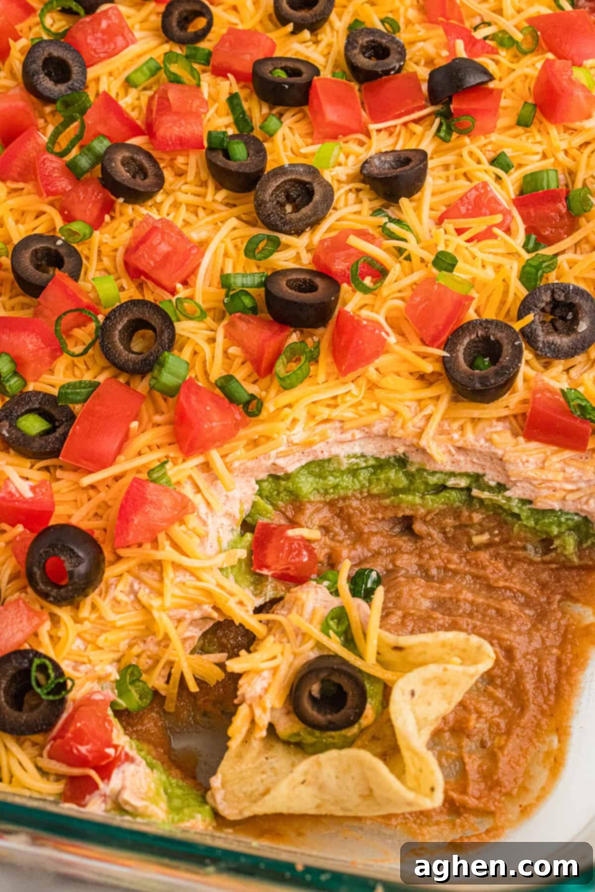 Seven Layer Taco Fiesta 8 A scoop taken from a 7-layer taco dip made with bean dip and no cream cheese, revealing layers of beans, guacamole, and sour cream.