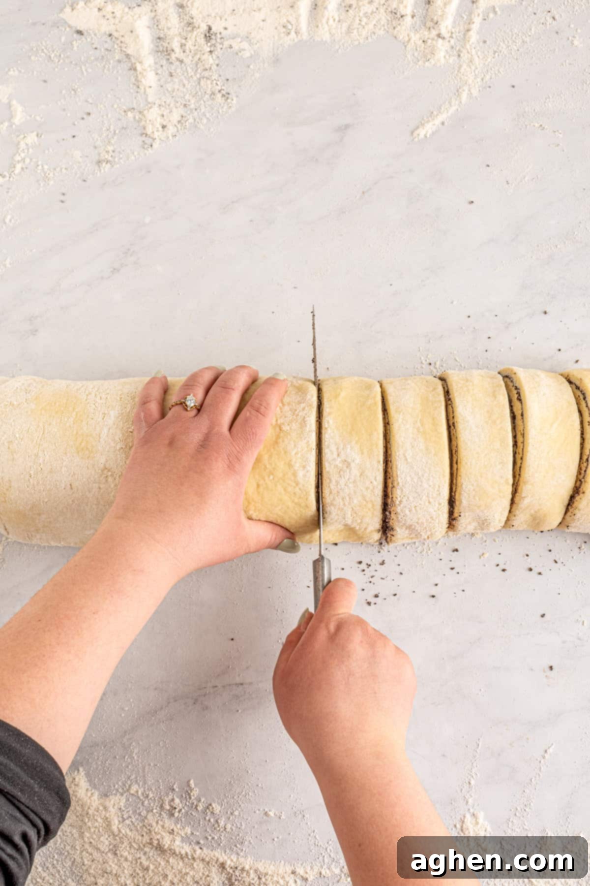 Cookies and Cream Dream Buns 10 Hands carefully slicing the rolled dough log into individual cinnamon rolls using a sharp knife.