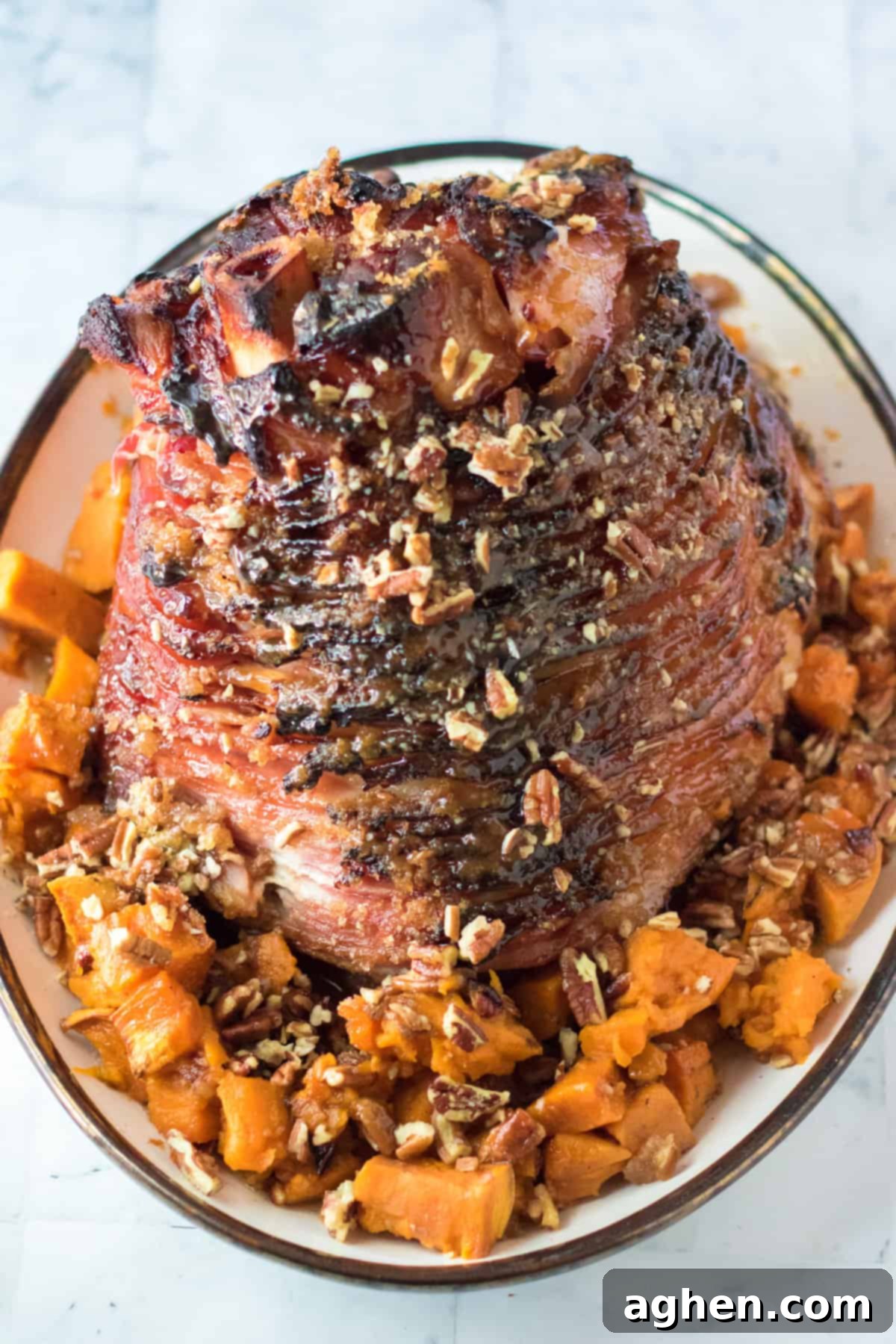 Decadent Pecan Praline Glazed Ham 11 Beautifully presented maple pecan glazed bone-in ham, surrounded by pecan-topped sweet potatoes, creating a festive holiday spread.