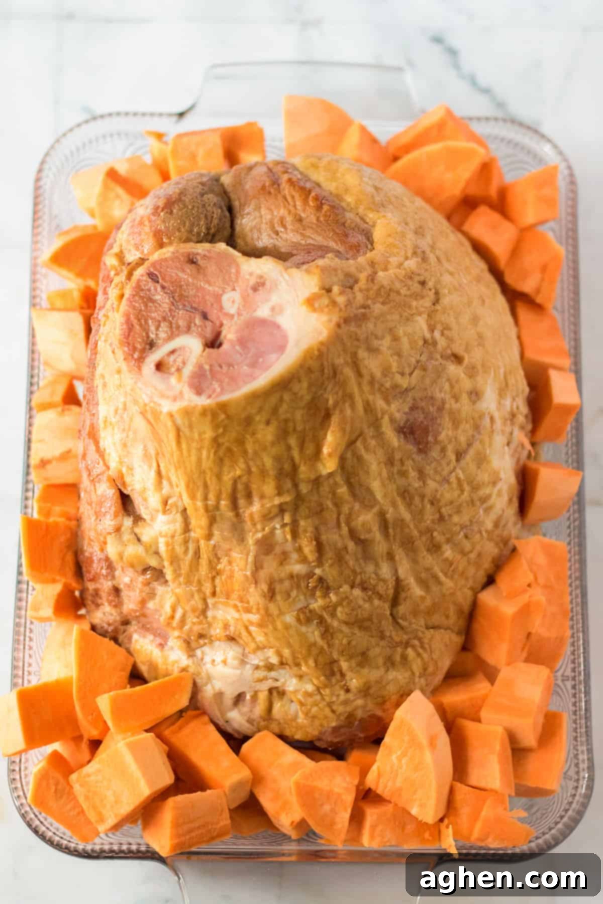 Decadent Pecan Praline Glazed Ham 5 Bone-in spiral ham placed in a baking dish, surrounded by chopped sweet potatoes, ready for the oven.