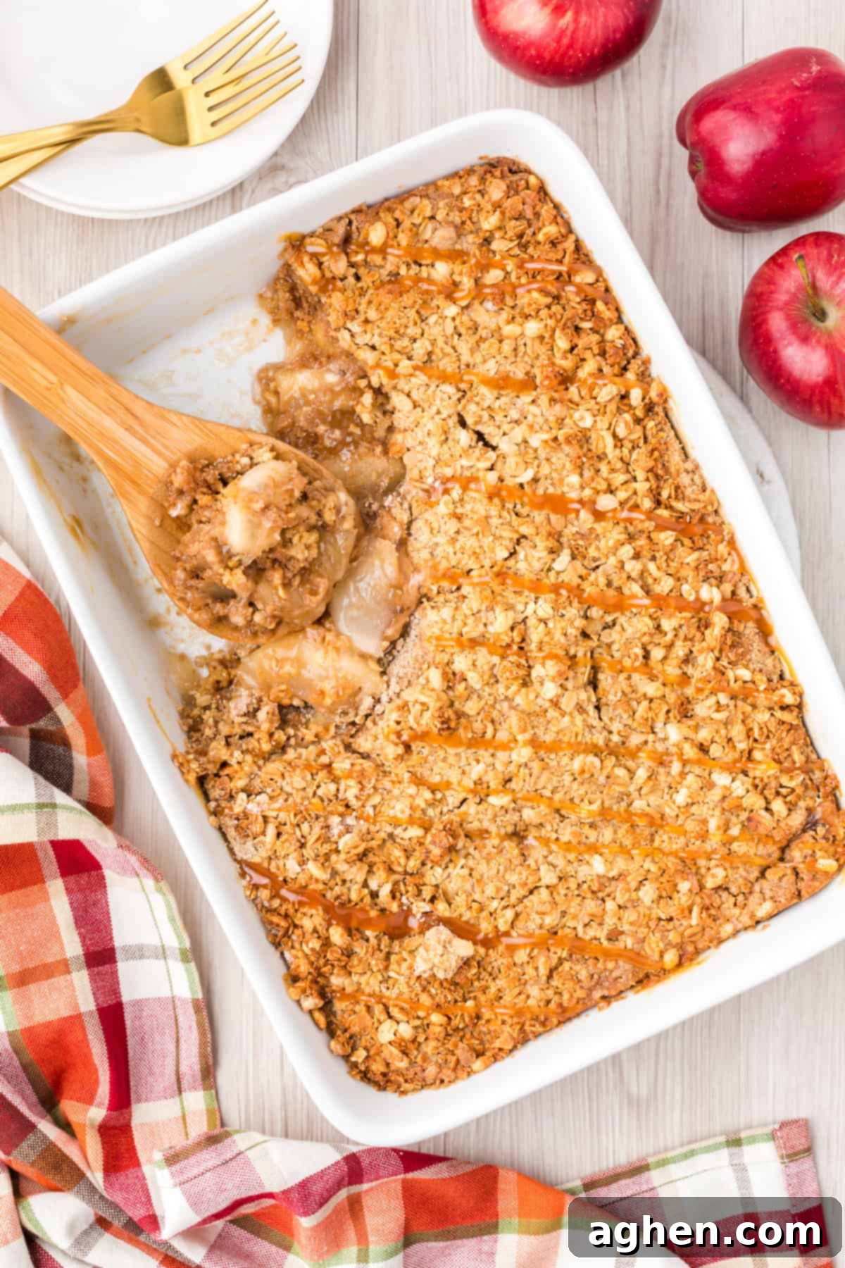 Apple crisp in 9 x 13 baking dish with caramel drizzled on top and a wooded spoon leaning in the removed portion.