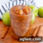 Apple pie filling in a wide mouth mason jar with cinnamon sticks and apples around it.