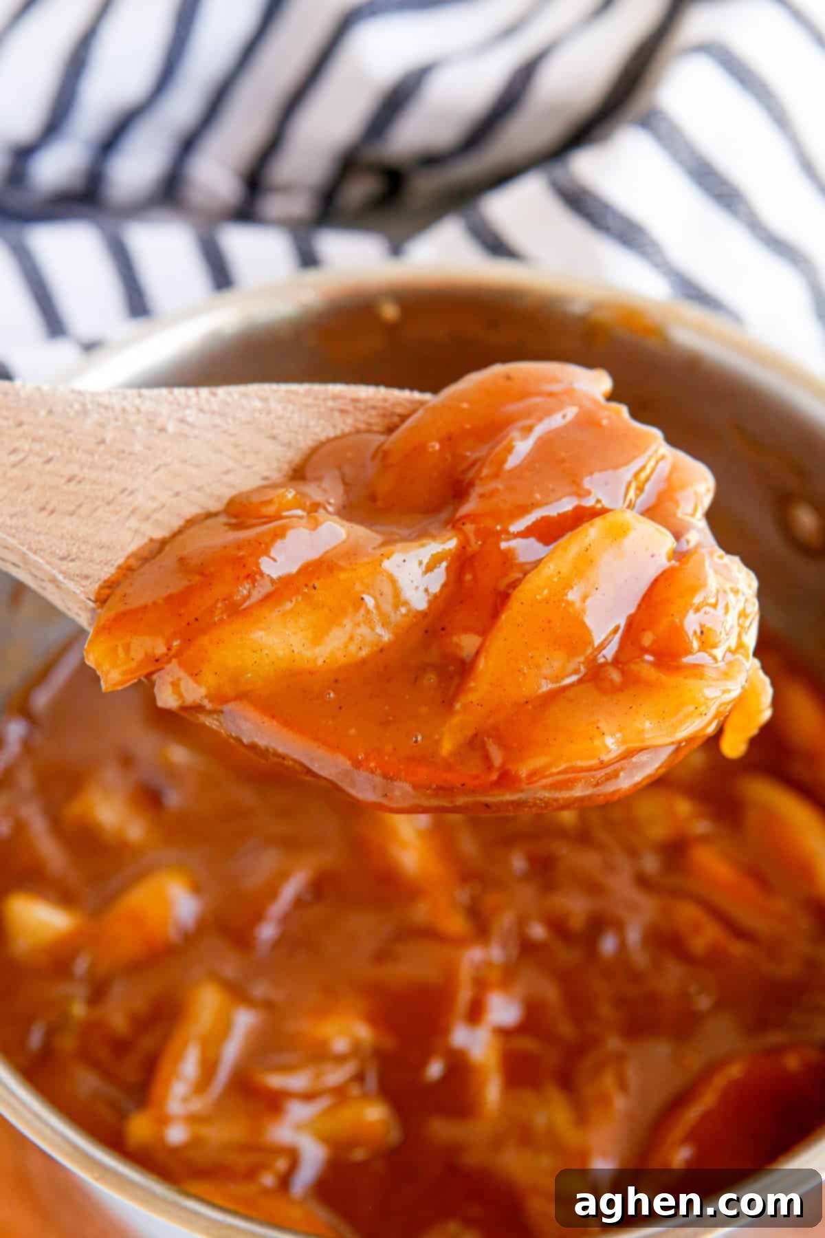 Wooden spoon lifting perfectly cooked homemade apple pie filling out of a pot on the stovetop.