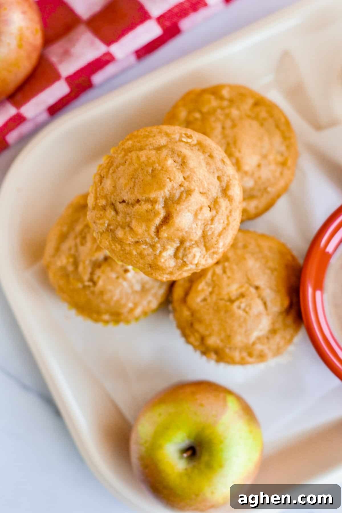 Apple oat muffins on lunch tray with fresh apple besides them.