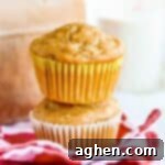 One apple muffin on top of another apple muffin in front of a brown paper bag.