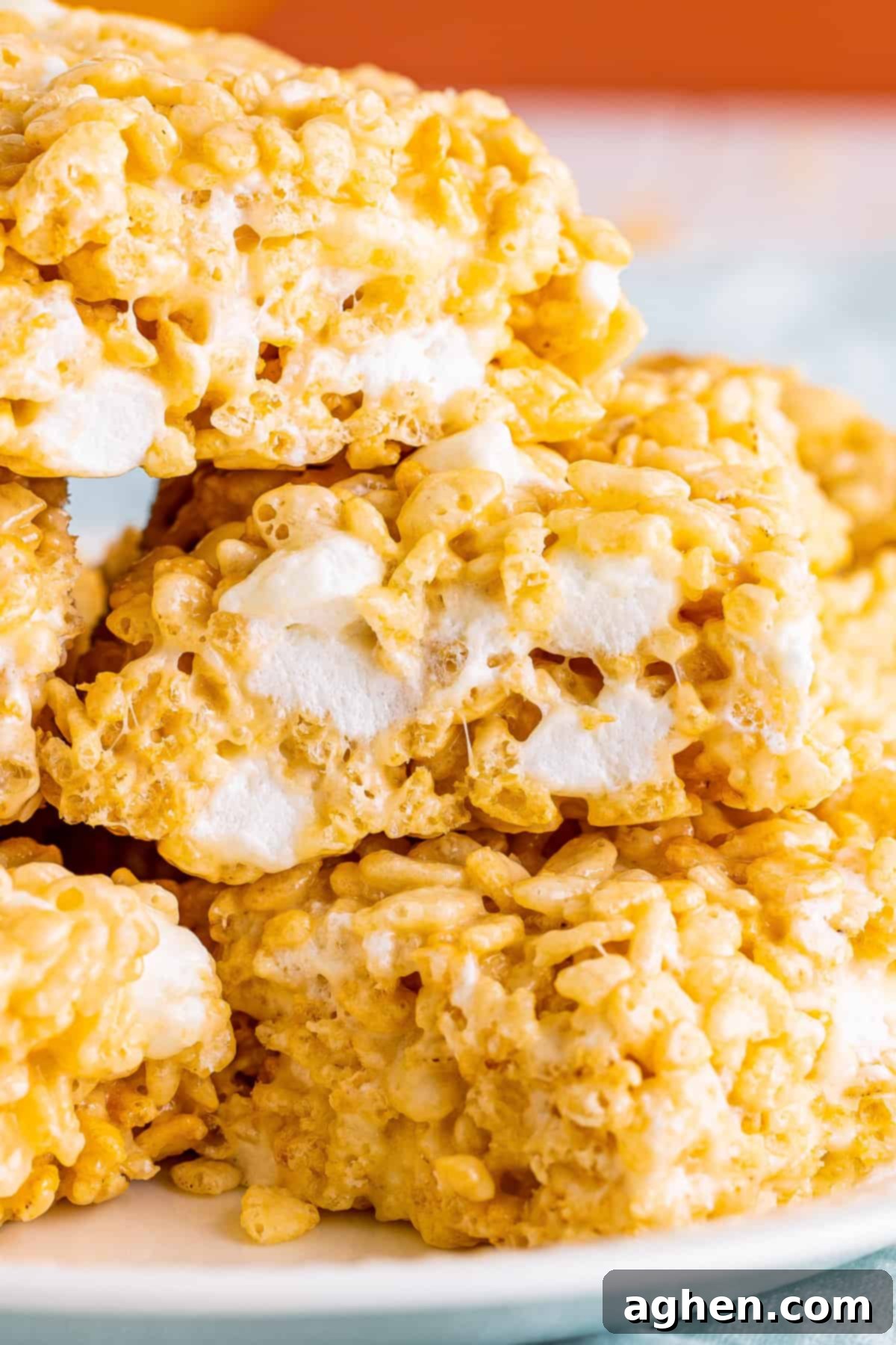 A close-up image of fluffy, marshmallow-filled Rice Krispies Treats stacked on a plate, highlighting their soft and chewy texture.