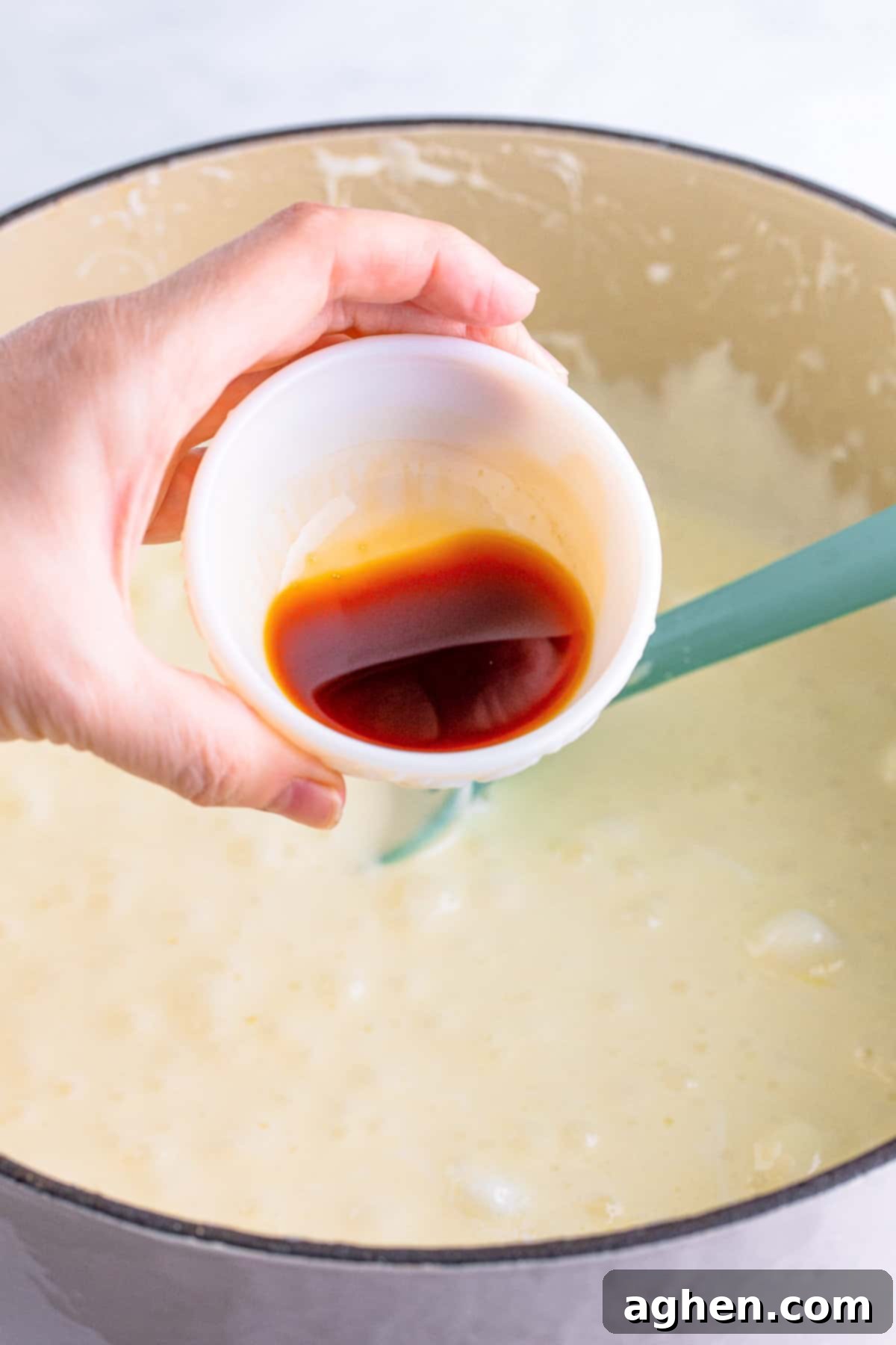 Pure vanilla extract being poured into the warm, melted marshmallow mixture in a Dutch oven, adding essential flavor.