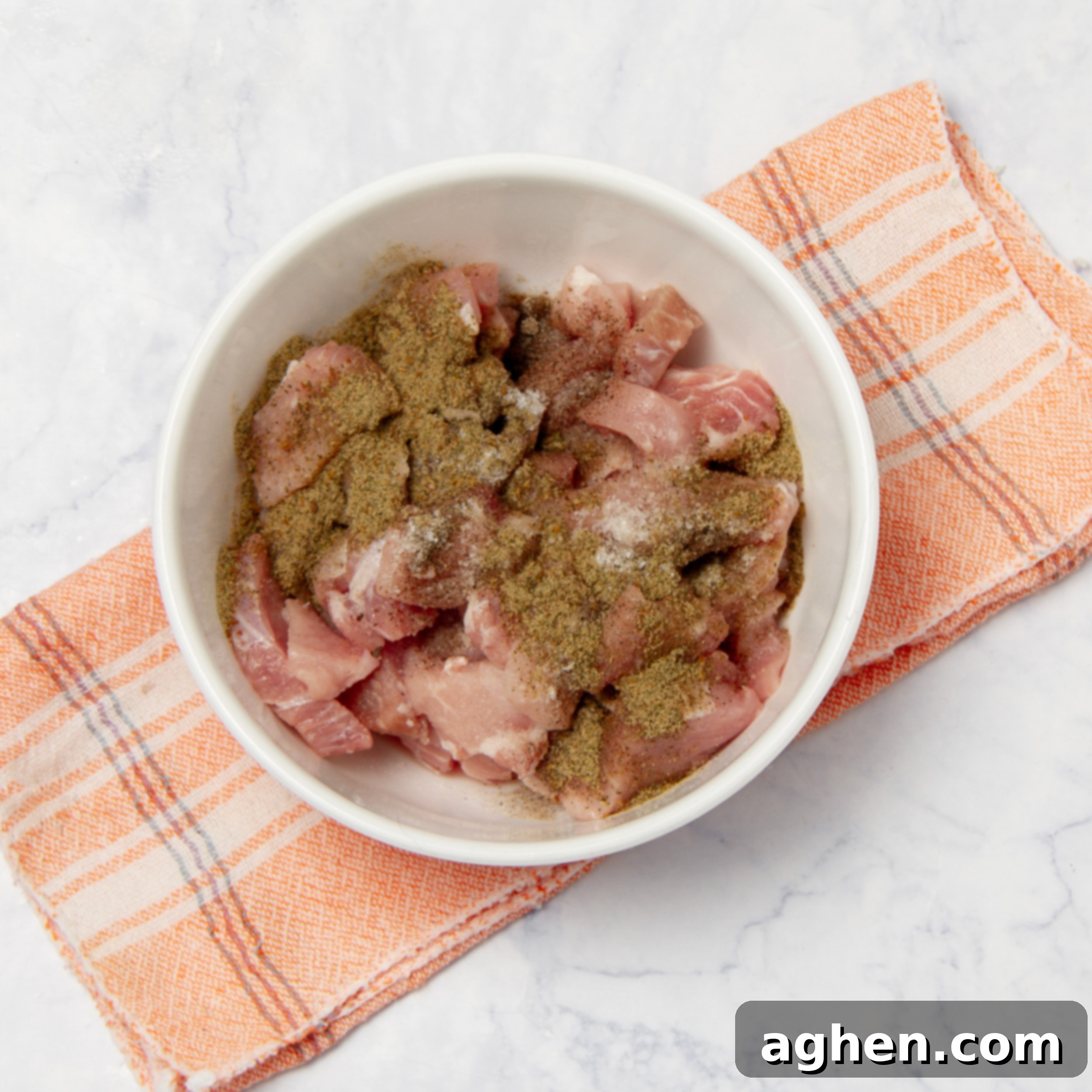 Cubed pork with seasonings in a small bowl. 