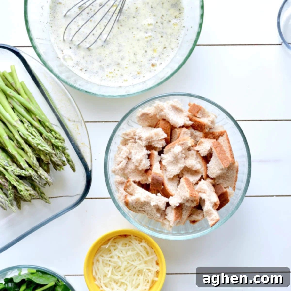 Hands arranging sliced bread and asparagus in a baking dish before pouring the egg custard over them for a casserole.