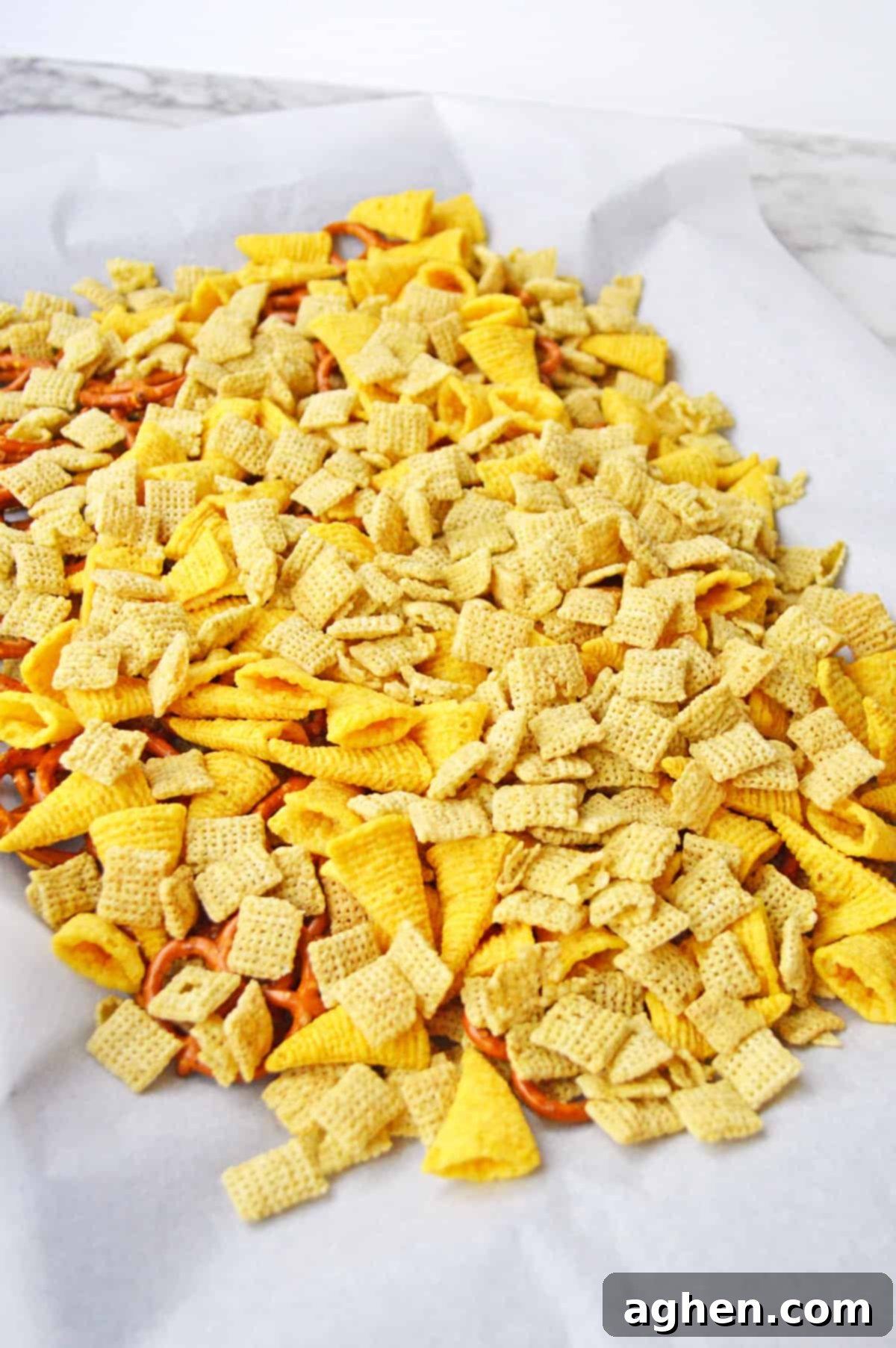 Chex cereal, Bugles, and mini pretzel twists mixed together evenly on a parchment-lined baking sheet, ready for the caramel coating.