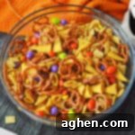A festive Halloween Chex Mix recipe with pretzels, Chex cereal, Bugles, M&Ms, and Reese's Pieces, displayed in a small bowl.