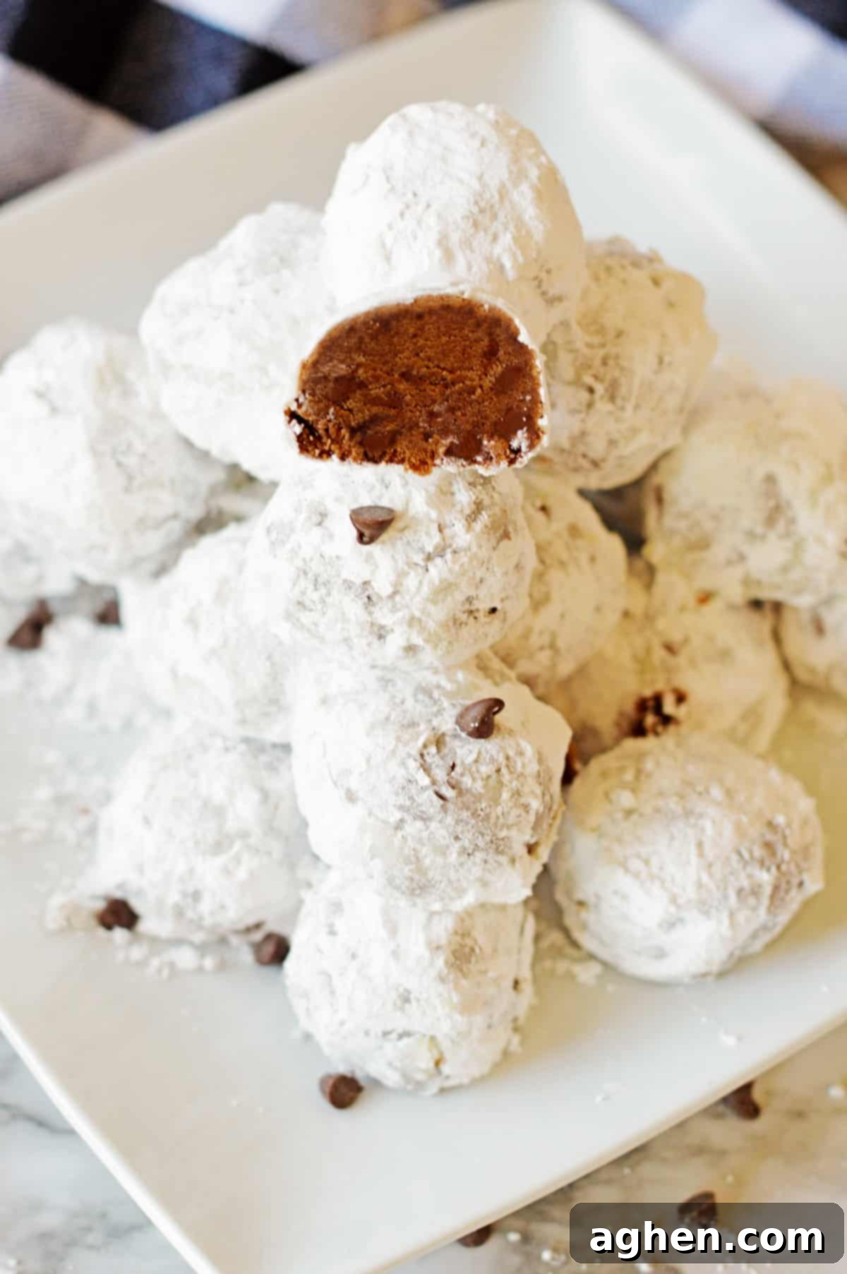 Decadent Double Chocolate Snowballs 2 Double chocolate snowball cookies stacked on a white plate with one cookie cut in half to show the rich chocolate interior packed with mini chocolate chips, highlighting their indulgent texture.