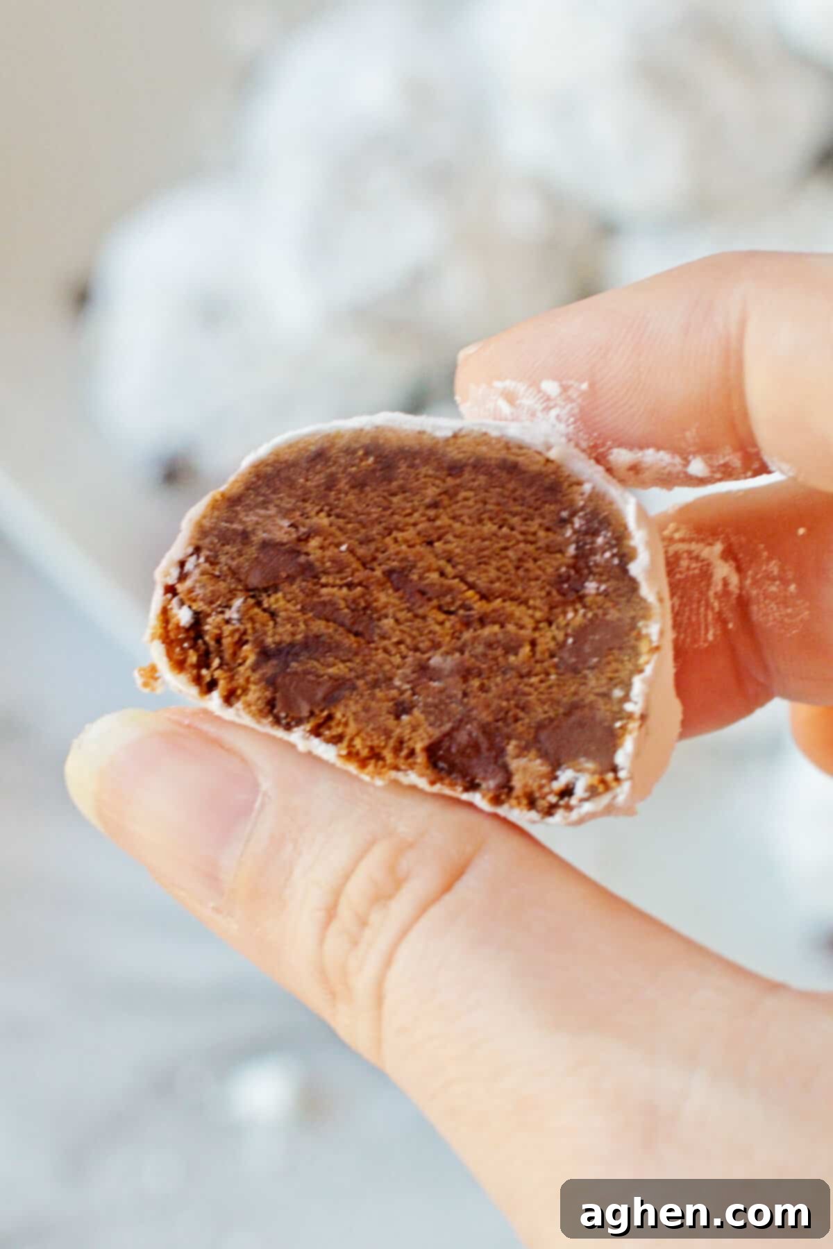 Decadent Double Chocolate Snowballs 11 A woman's hand gently holding a double chocolate snowball cookie, showing off its rich interior with mini chocolate chips and its perfect powdered sugar coating.