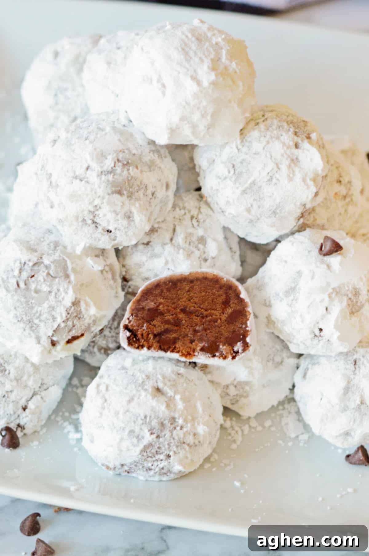 Decadent Double Chocolate Snowballs 3 Chocolate snowballs artfully arranged on a white plate, with one cookie sliced in half to showcase its delightful chocolate interior.