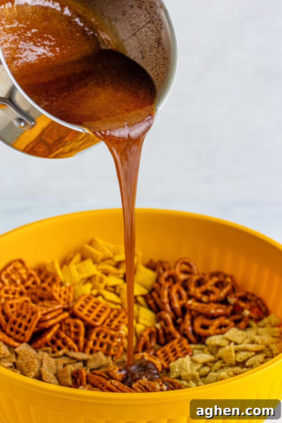 The rich cinnamon sugar and butter mixture being poured over the prepared Chex mix ingredients in a large bowl.