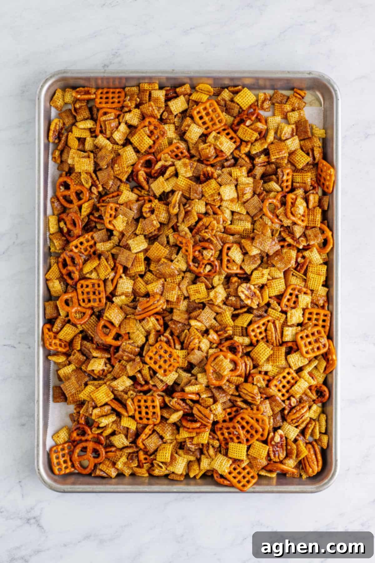 Cinnamon sugar coated Chex mix spread out evenly on a parchment-lined baking sheet, ready for baking.