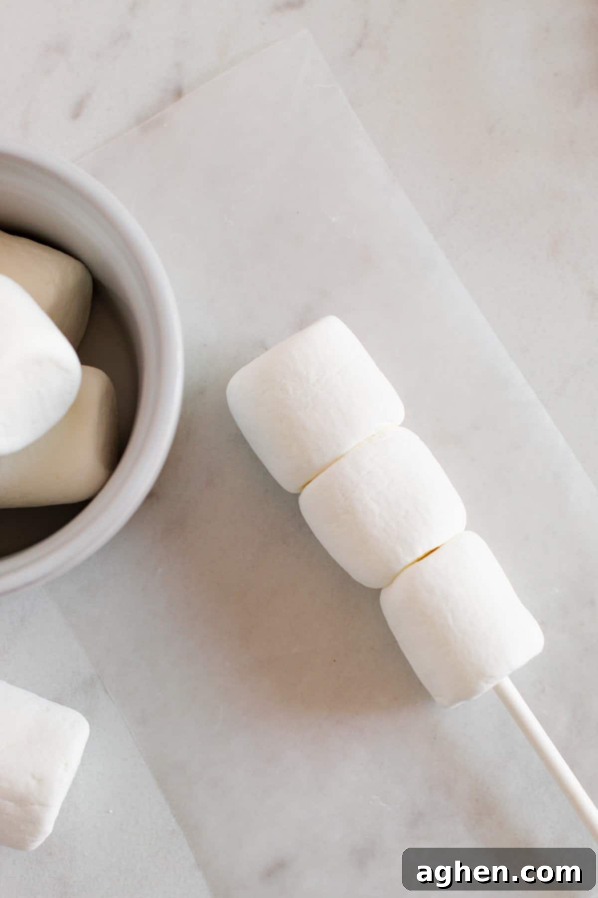 Three white marshmallows on end of white treat stick.
