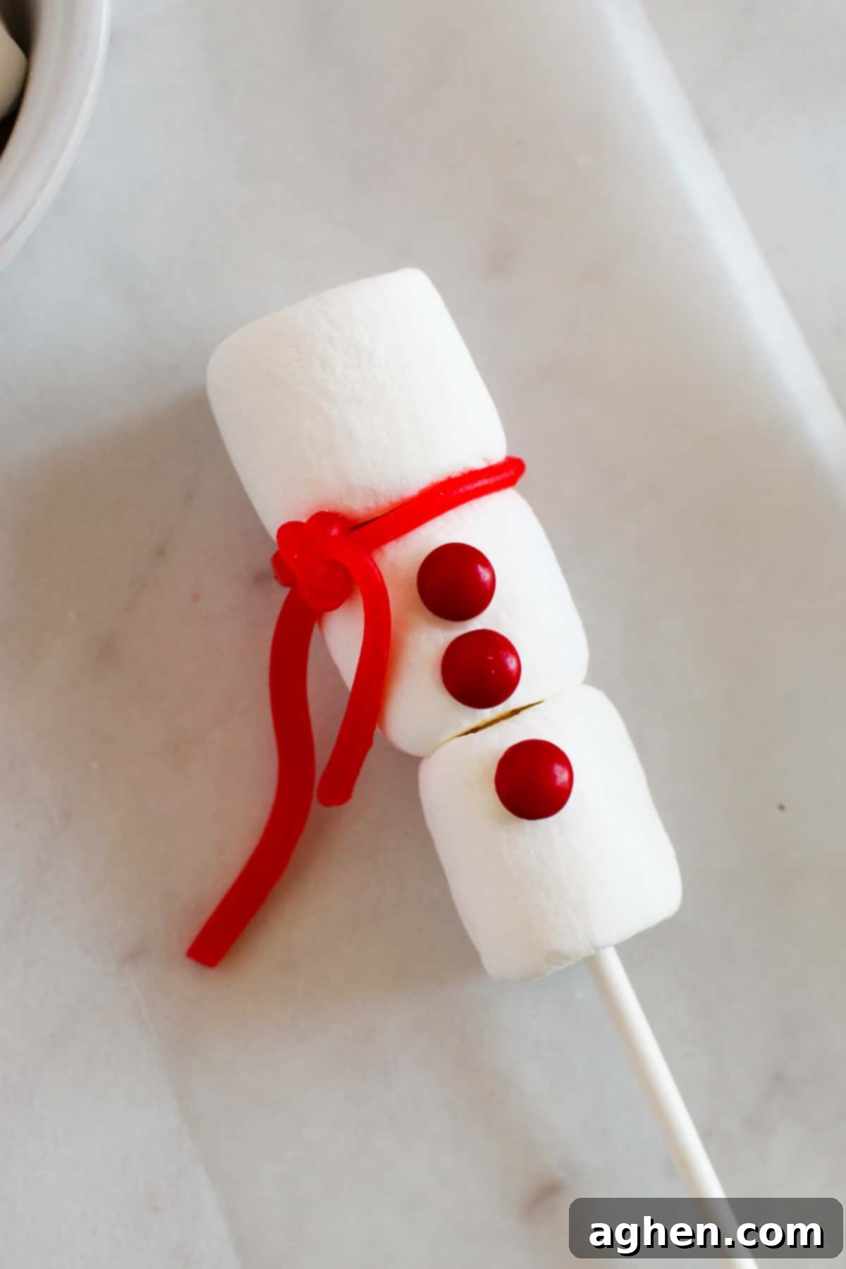 A piece of red candy has been tied between the top and middle marshmallow to make a scarf.