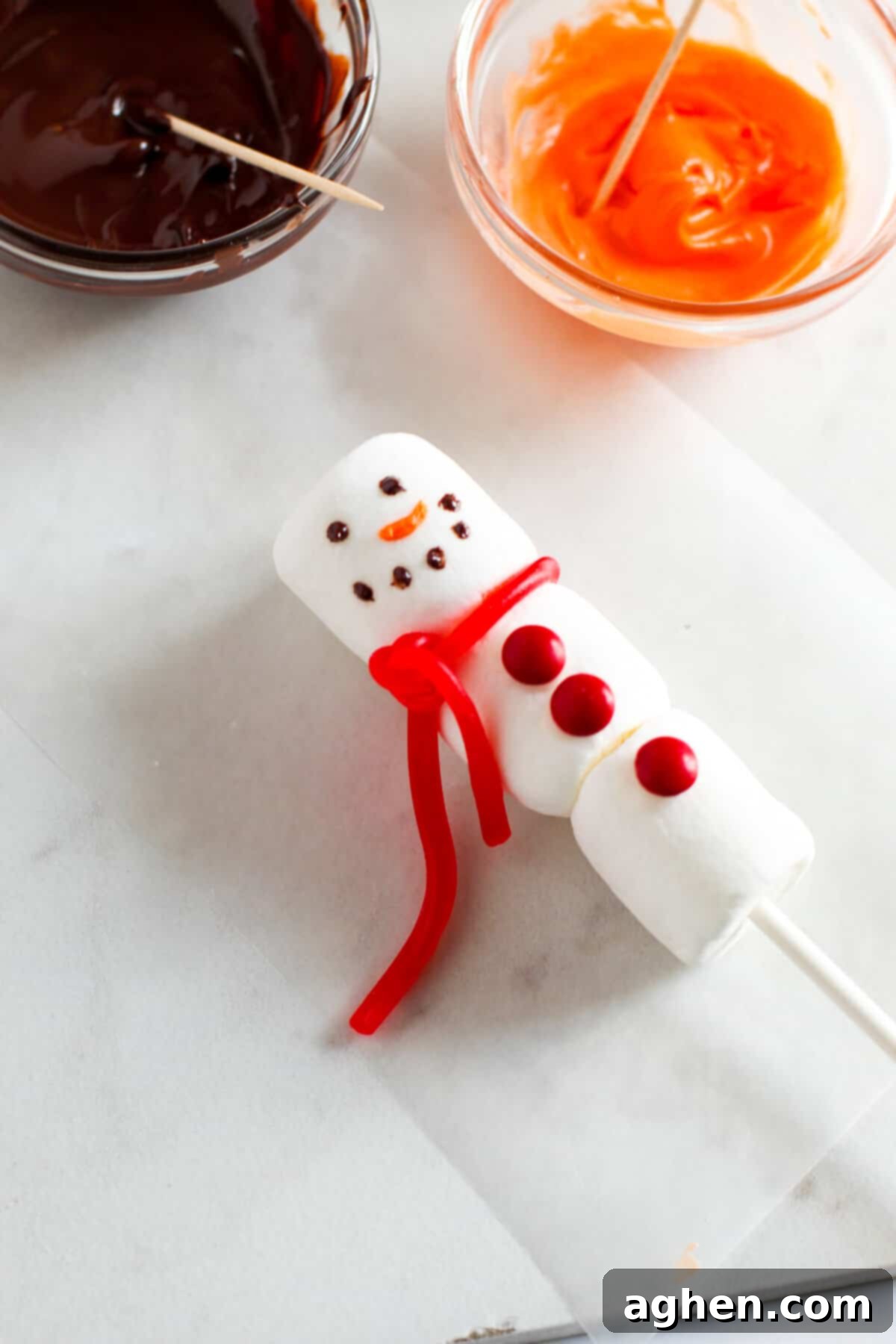 Dots of chocolate added on top marshmallow to make his eyes and mouth. Orange carrot added for nose.