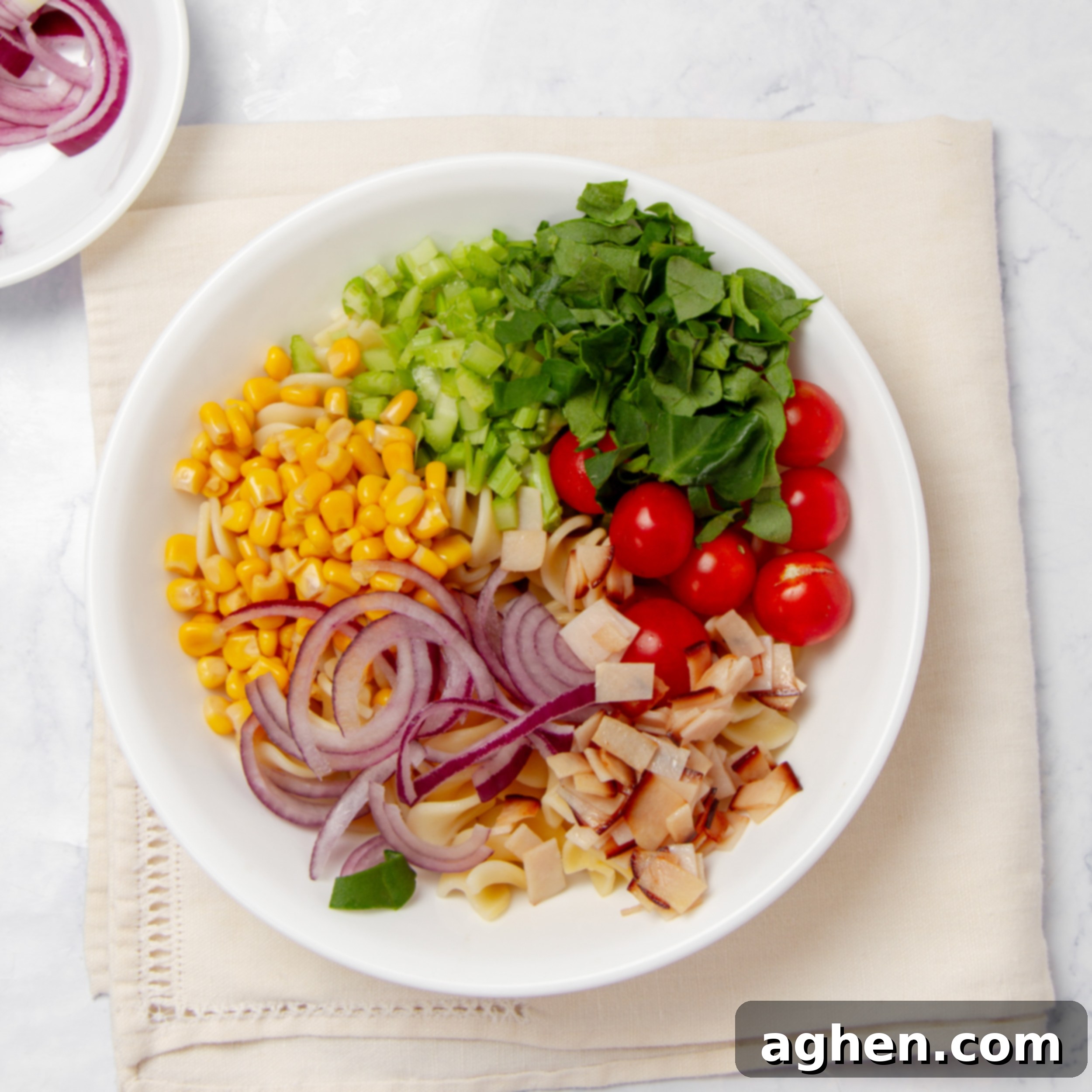 A vibrant assortment of prepped vegetables, fresh herbs, and crumbled smoked turkey ham in a bowl, meticulously prepared and ready to be mixed into the Spring Chicken Pasta Salad.