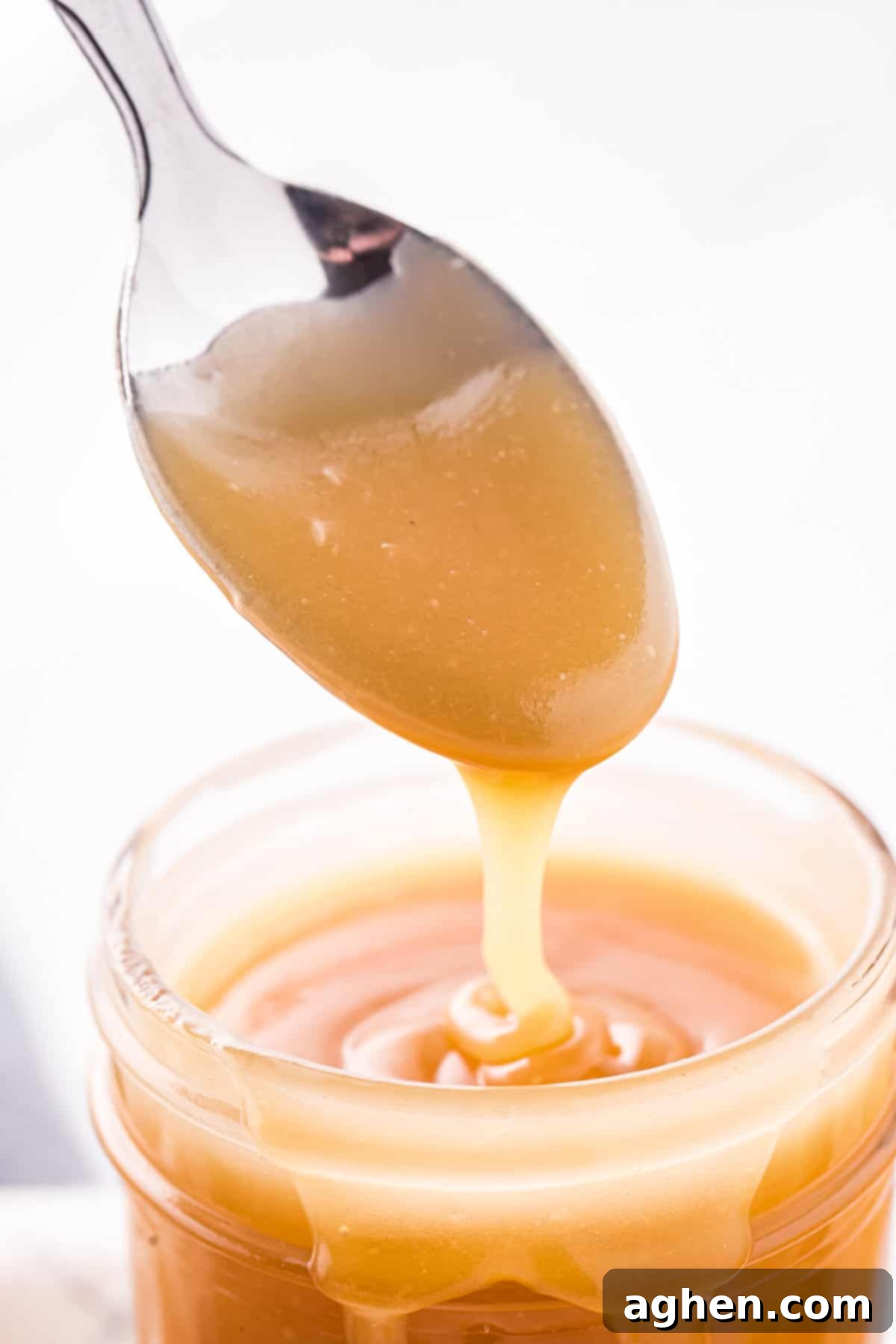 Perfect Homemade Caramel 9 Spoon drizzling caramel sauce into glass jar.
