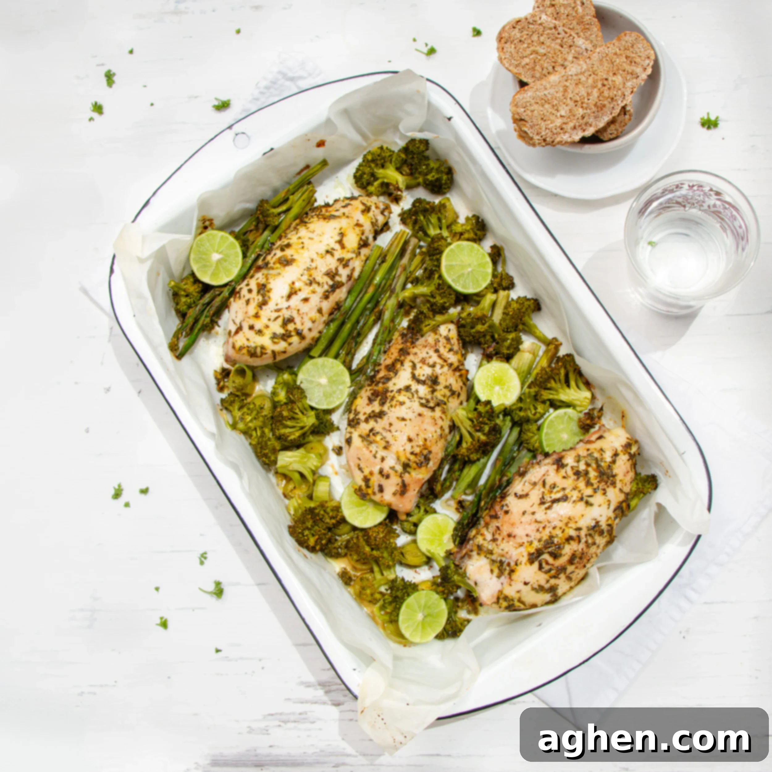 Herbaceous tarragon chicken with asparagus in a serving dish with bread and water on the side. 