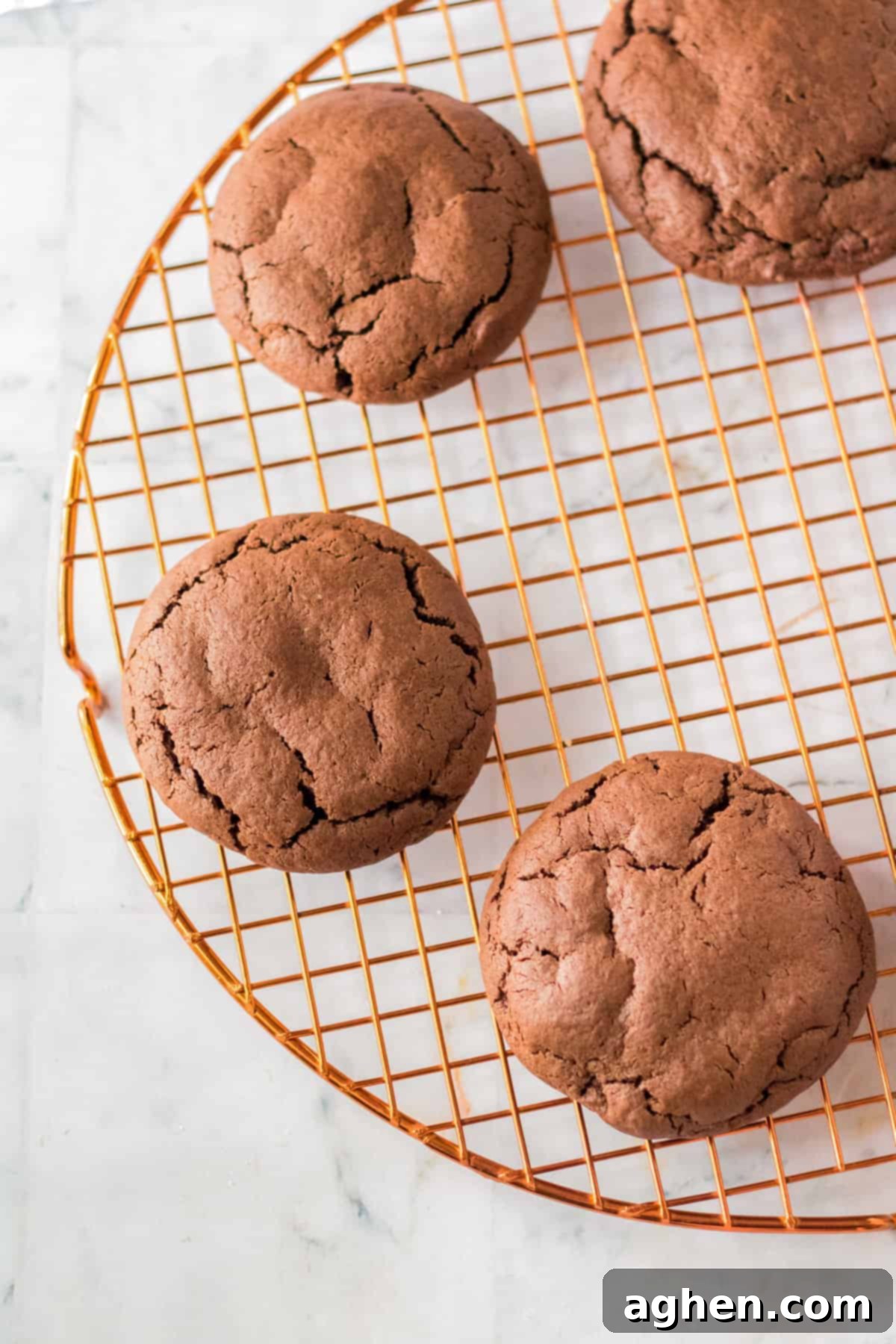 Freshly baked large, thick chocolate cookies cooling on a brass wire rack, awaiting their festive toppings.
