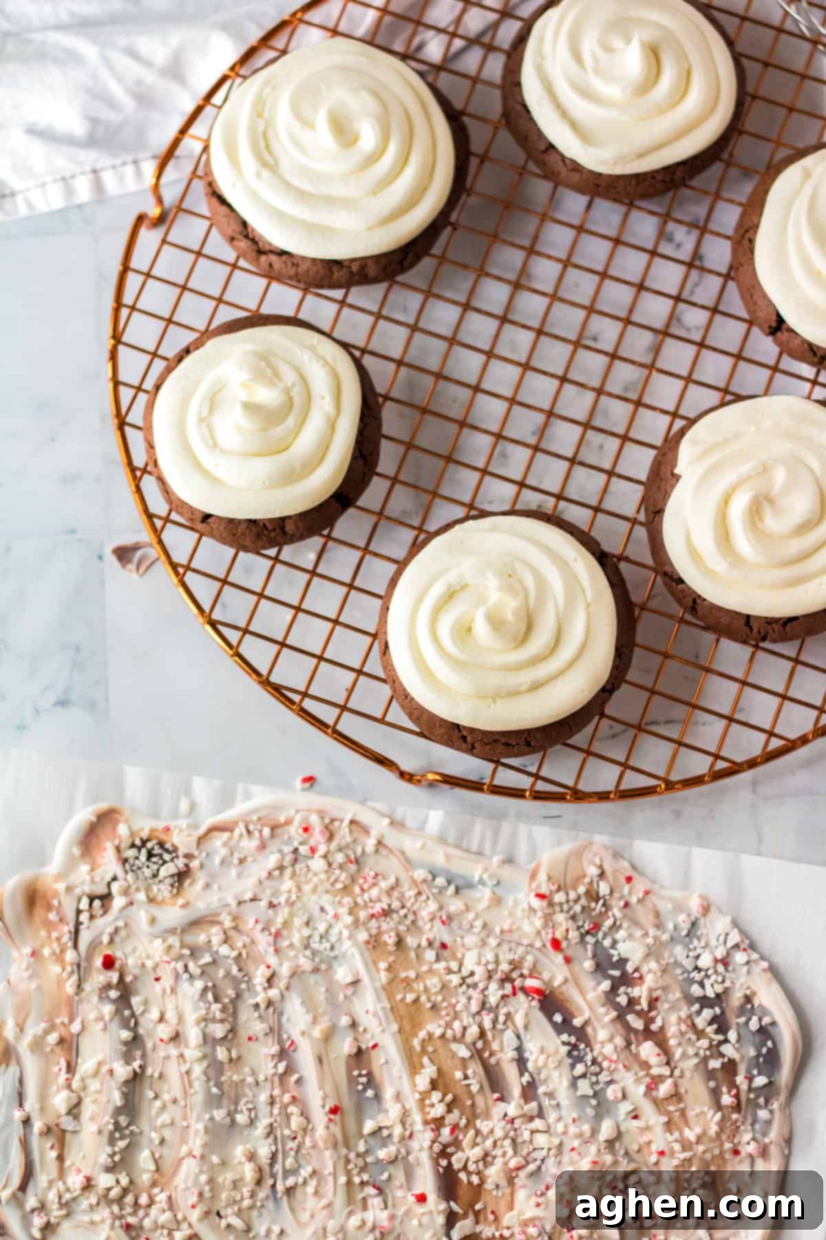 Frosted chocolate cookies on a wire rack alongside fresh homemade peppermint bark on parchment paper, ready for final assembly.