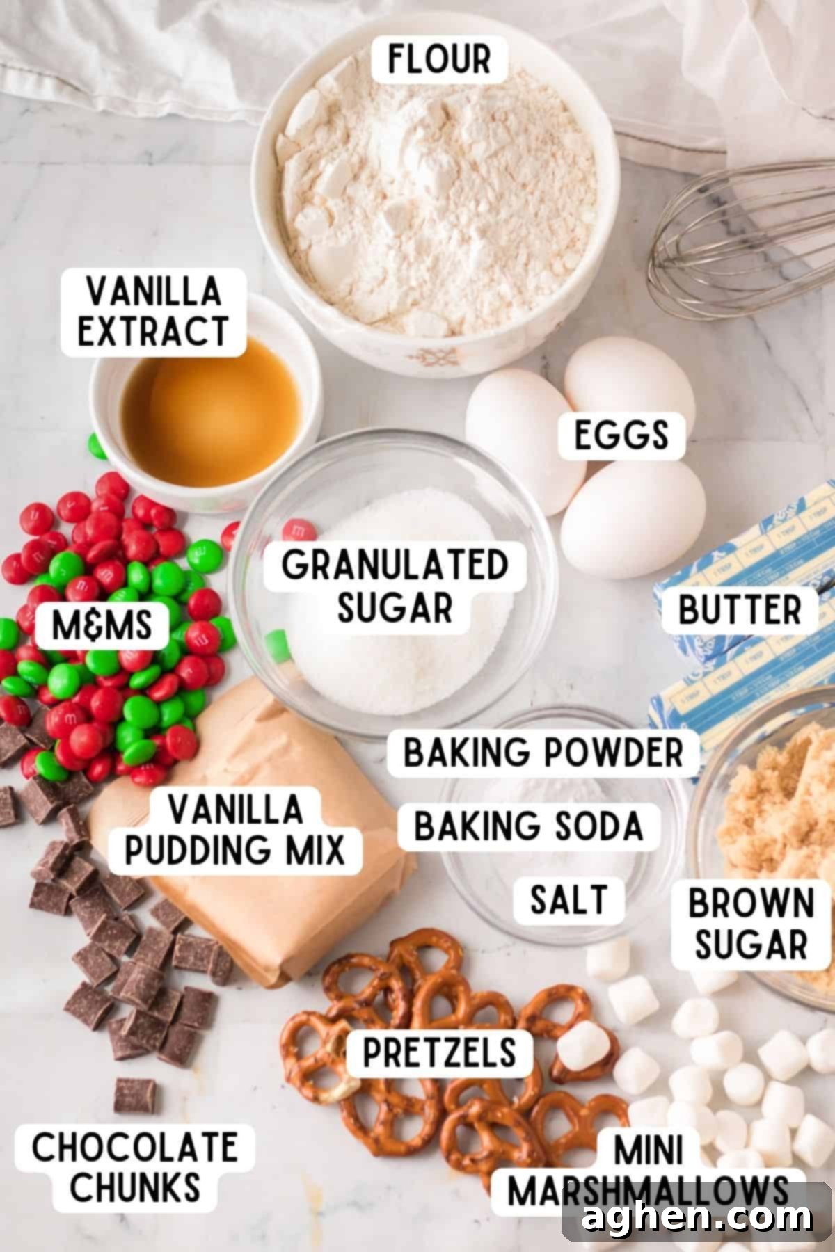 A collection of ingredients laid out for making kitchen sink Christmas cookies, including butter, sugars, eggs, flour, pudding mix, chocolate, M&Ms, marshmallows, and pretzels.
