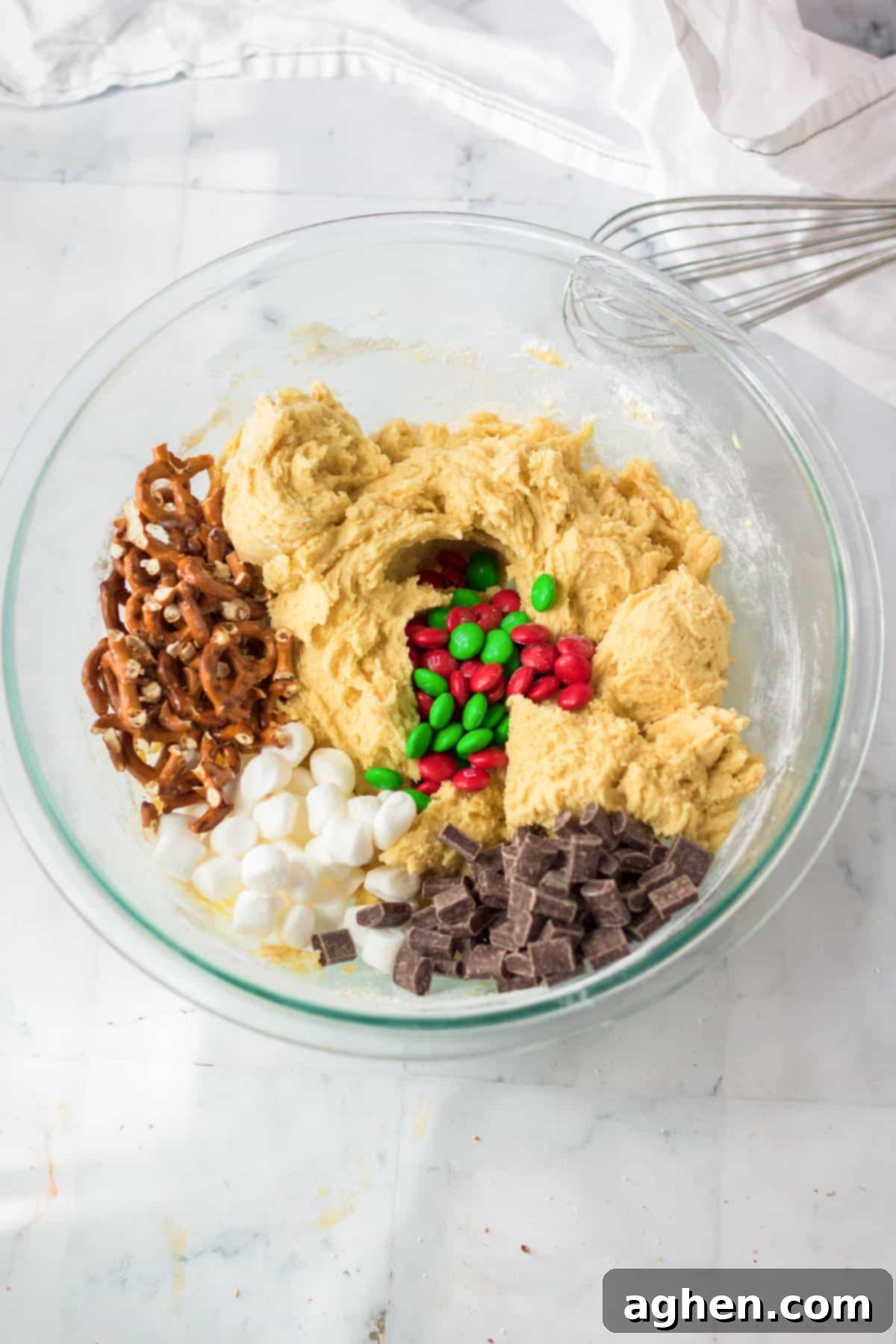 A bowl of rich cookie dough, generously mixed with festive red and green M&Ms, fluffy mini marshmallows, crunchy pretzels, and decadent chocolate chunks.
