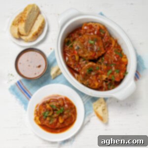 Juicy and tender Swiss Steak in stewed vegetable sauce. An individual serving stis on a plate next to the serving platter with brea and extra sauce on the side.