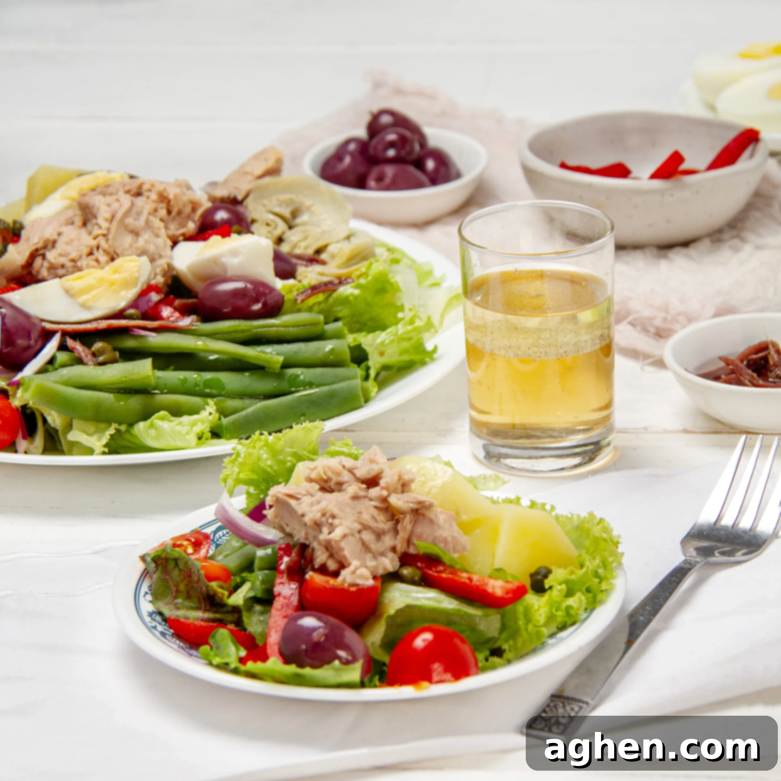 Fresh and flavorful Niçoise Salad on a plate with extra salad and a glass of juice on the side.