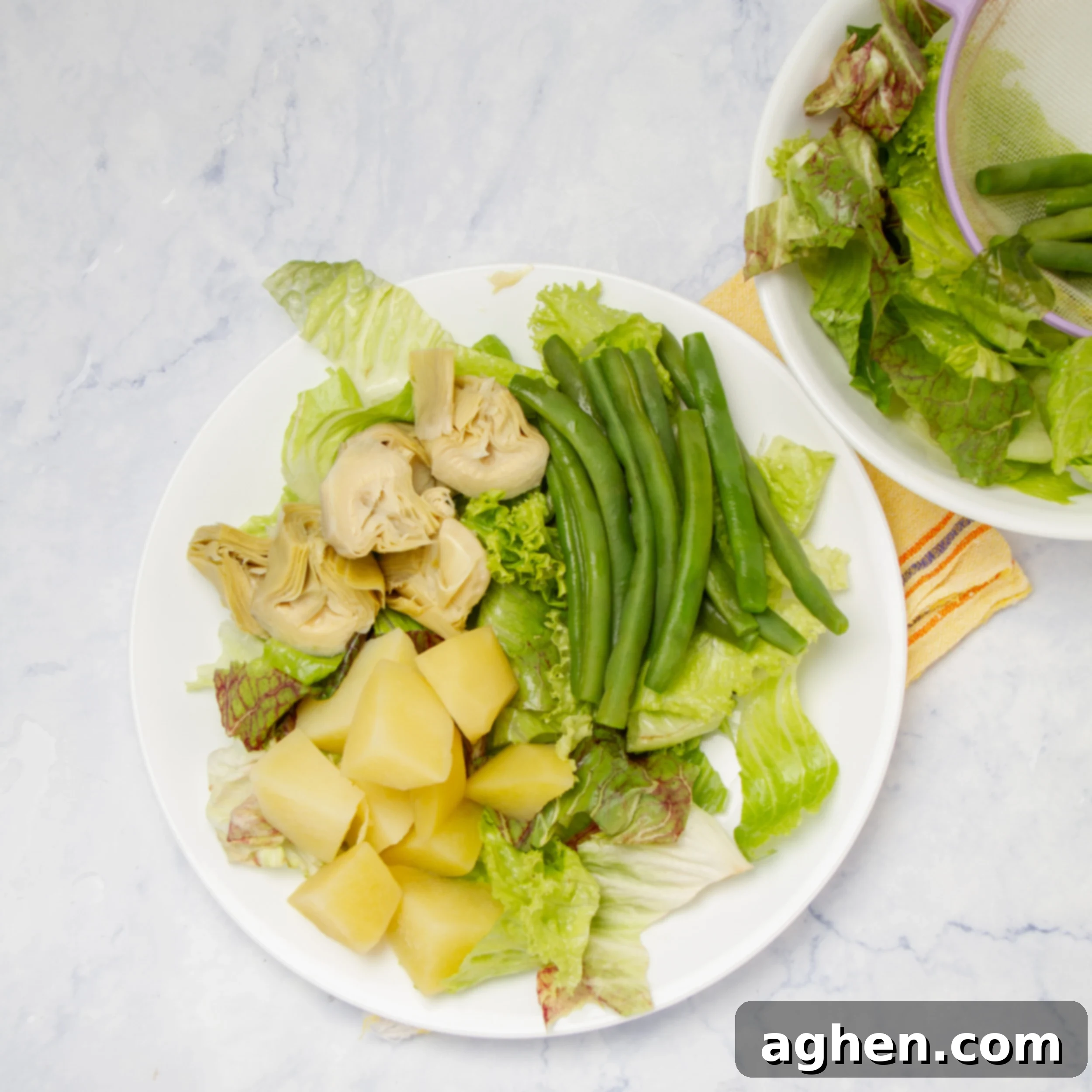Potatoes, green beans, and artichokes atop a bed of lettuce on a plate.