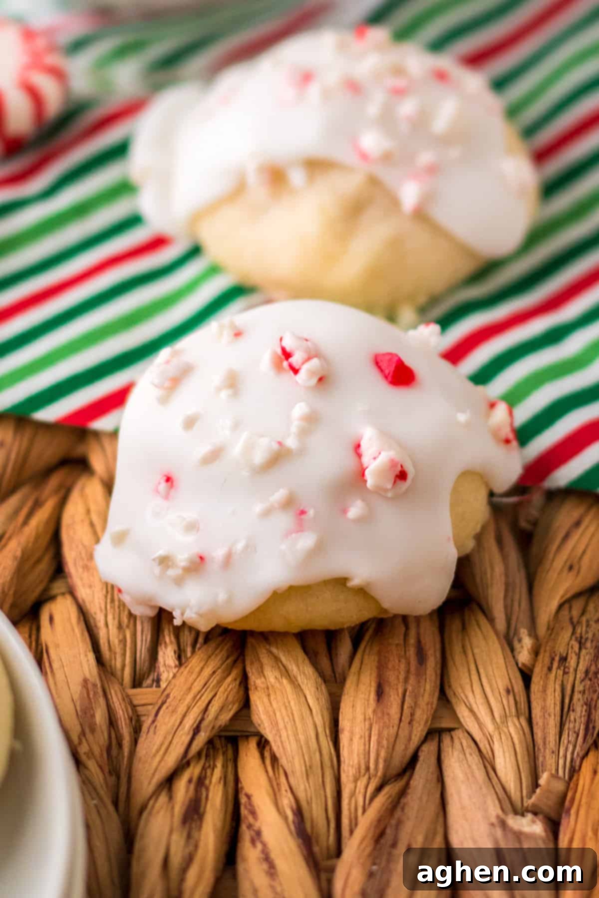 Close-up of a stack of iced peppermint cookies on a festive holiday napkin, highlighting the crushed candy cane topping.