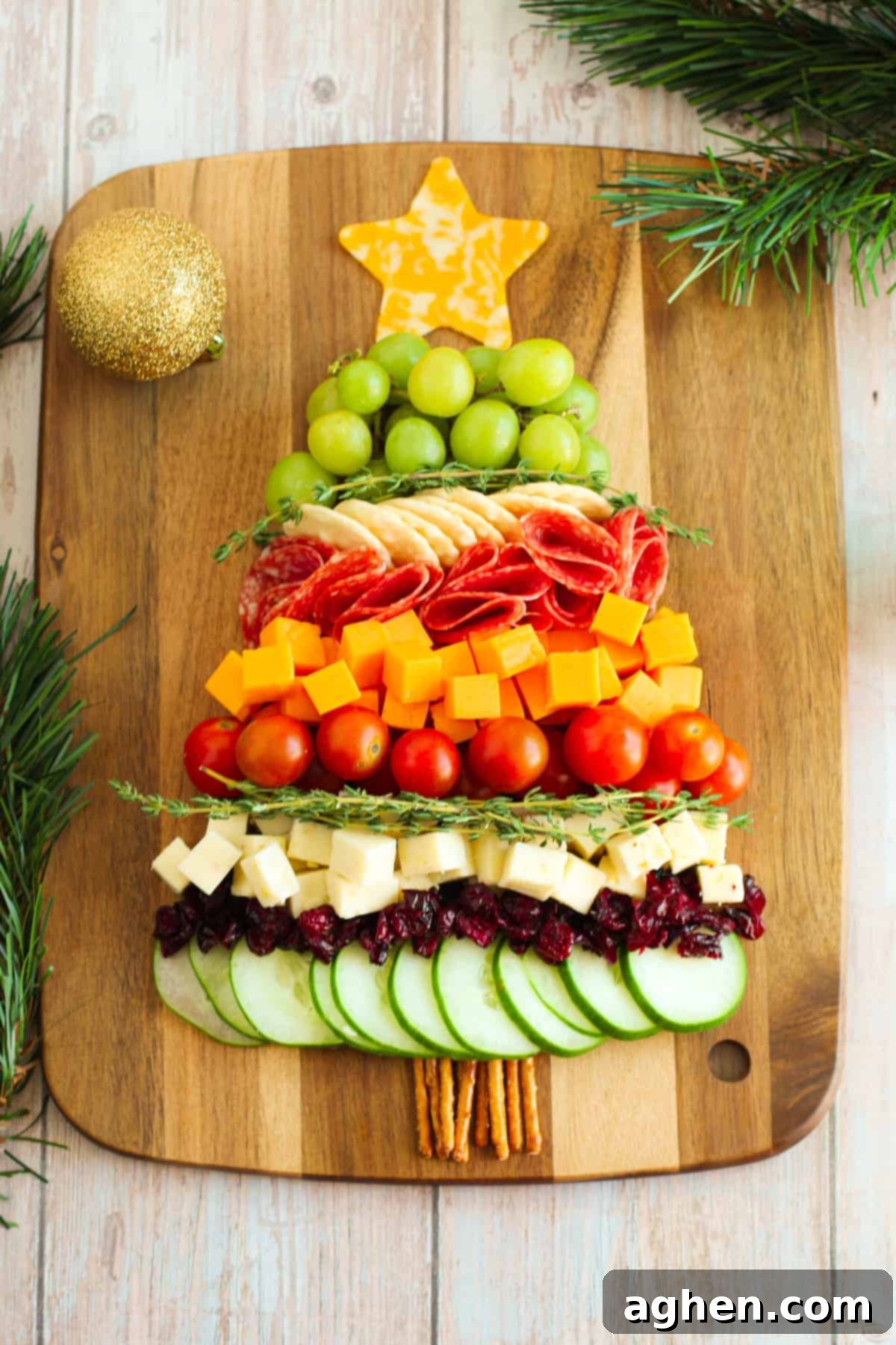 Charcuterie board shaped like a Christmas tree with an assortment of cheeses, cucumbers, tomatoes, grapes, salami, and other festive garnishes.